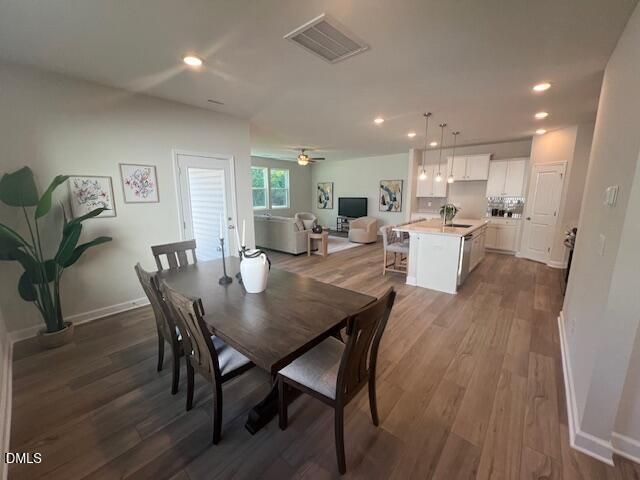 Open-concept dining area with wooden table and chairs adjoining living room and white kitchen island in The Preston A, Lillington, NC