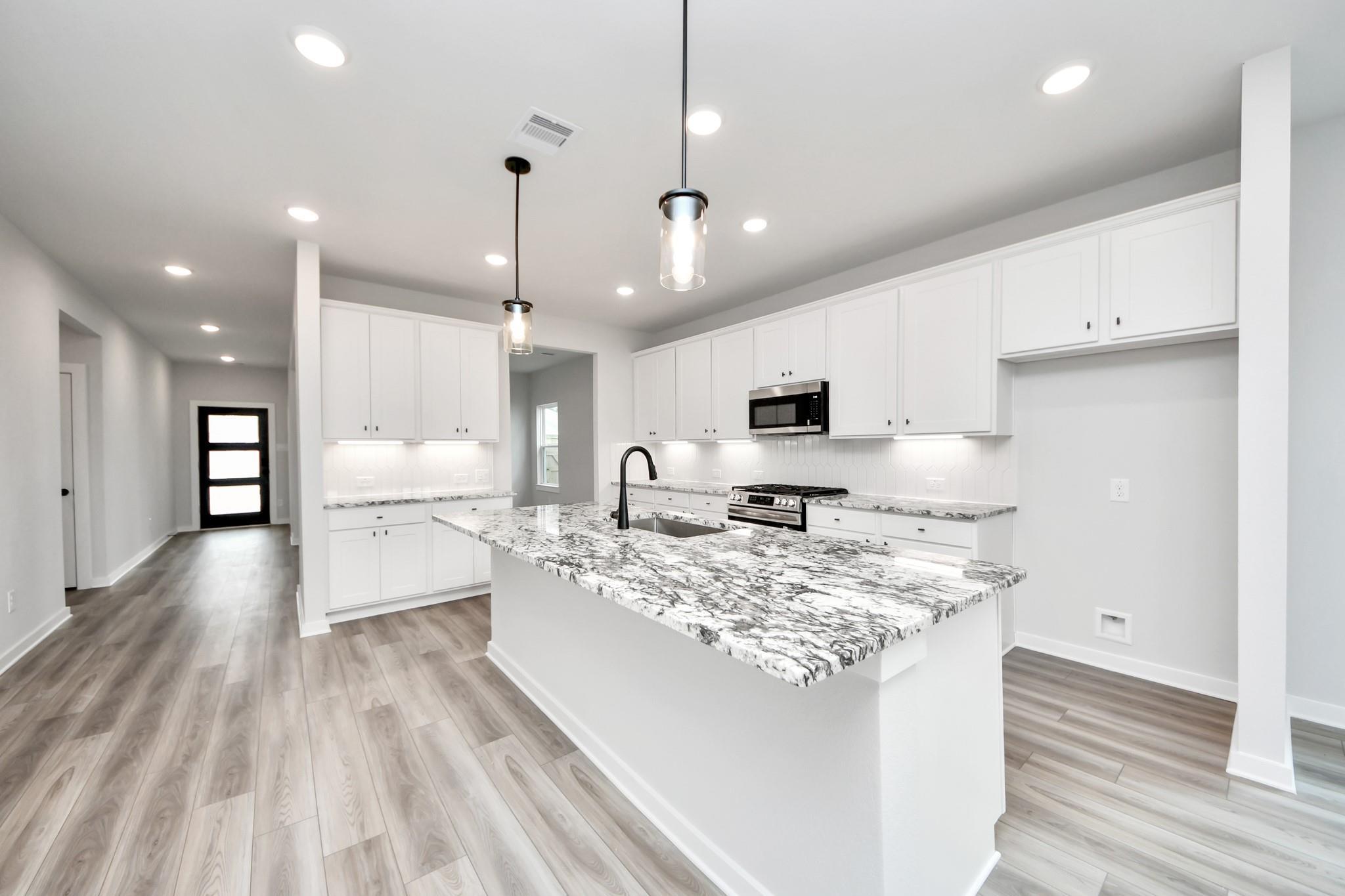 Modern kitchen with marble-look island, white cabinets, and wood flooring in The Sorrento E at Sundance Cove, Crosby, Texas.