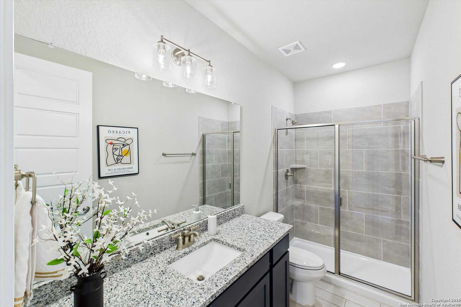 Modern bathroom with granite vanity, glass shower enclosure, and tiled walls in The Jennings H by Davidson Homes, Ladera, San Antonio