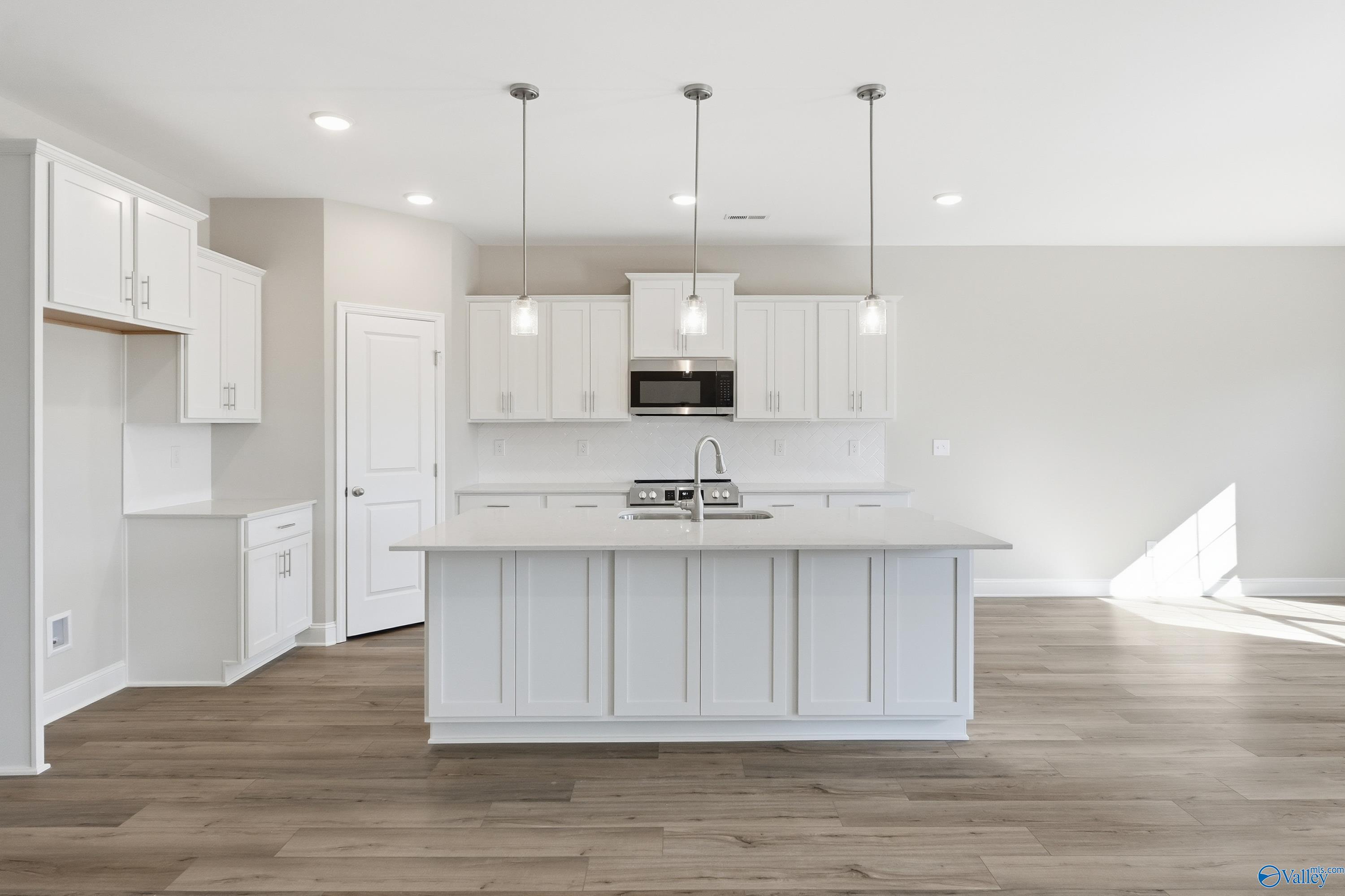 Modern white shaker kitchen with oversized island, stainless appliances, pendant lights, and hardwood floors in The Rockford by Davidson Homes, Harvest AL