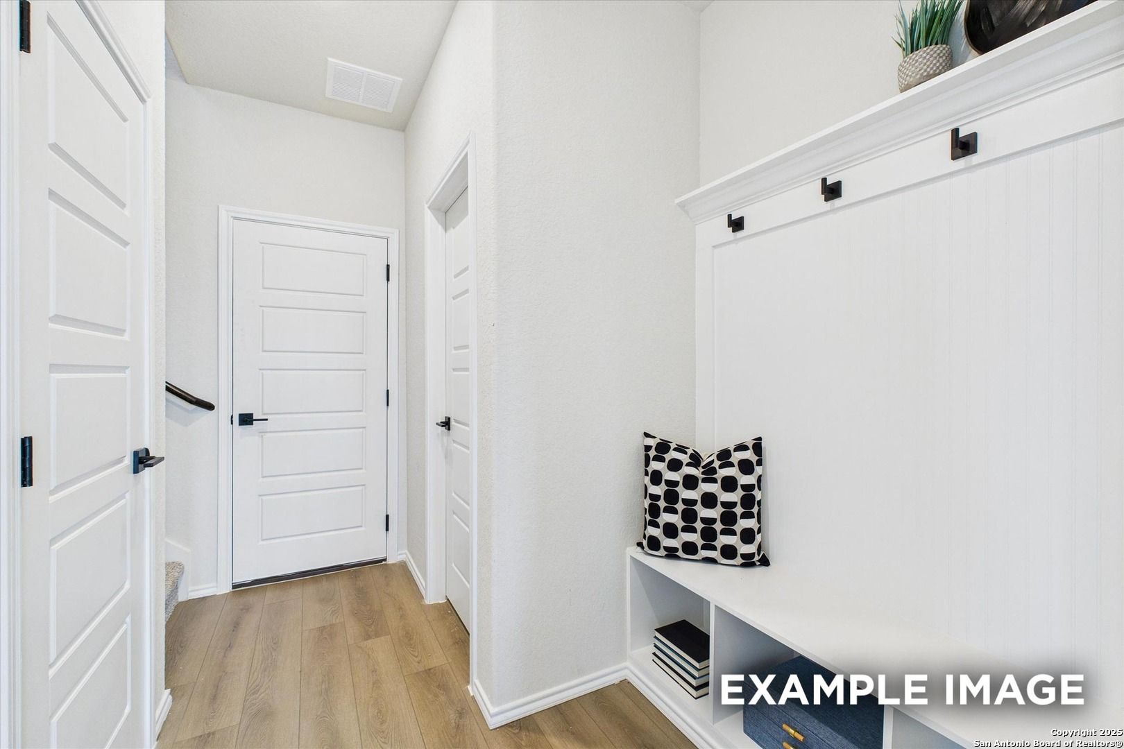 Bright entryway mudroom with built-in bench, patterned pillow, coat hooks, and shelves in Davidson Homes The Florence C, San Antonio