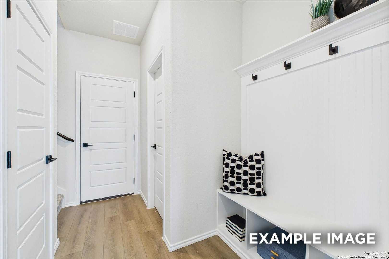 Bright entryway mudroom with built-in bench, patterned pillow, coat hooks, and shelves in Davidson Homes The Florence C, San Antonio