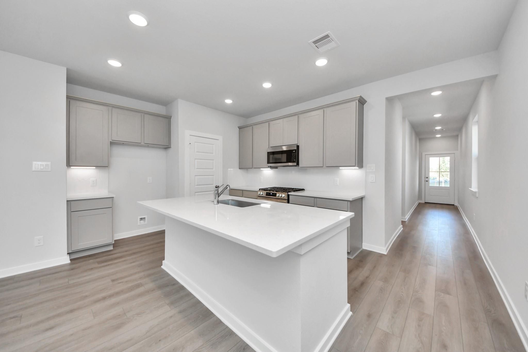 Modern kitchen with white island, gray cabinets, and light wood floors in The Colorado G home at Emberly, Beasley, Texas.