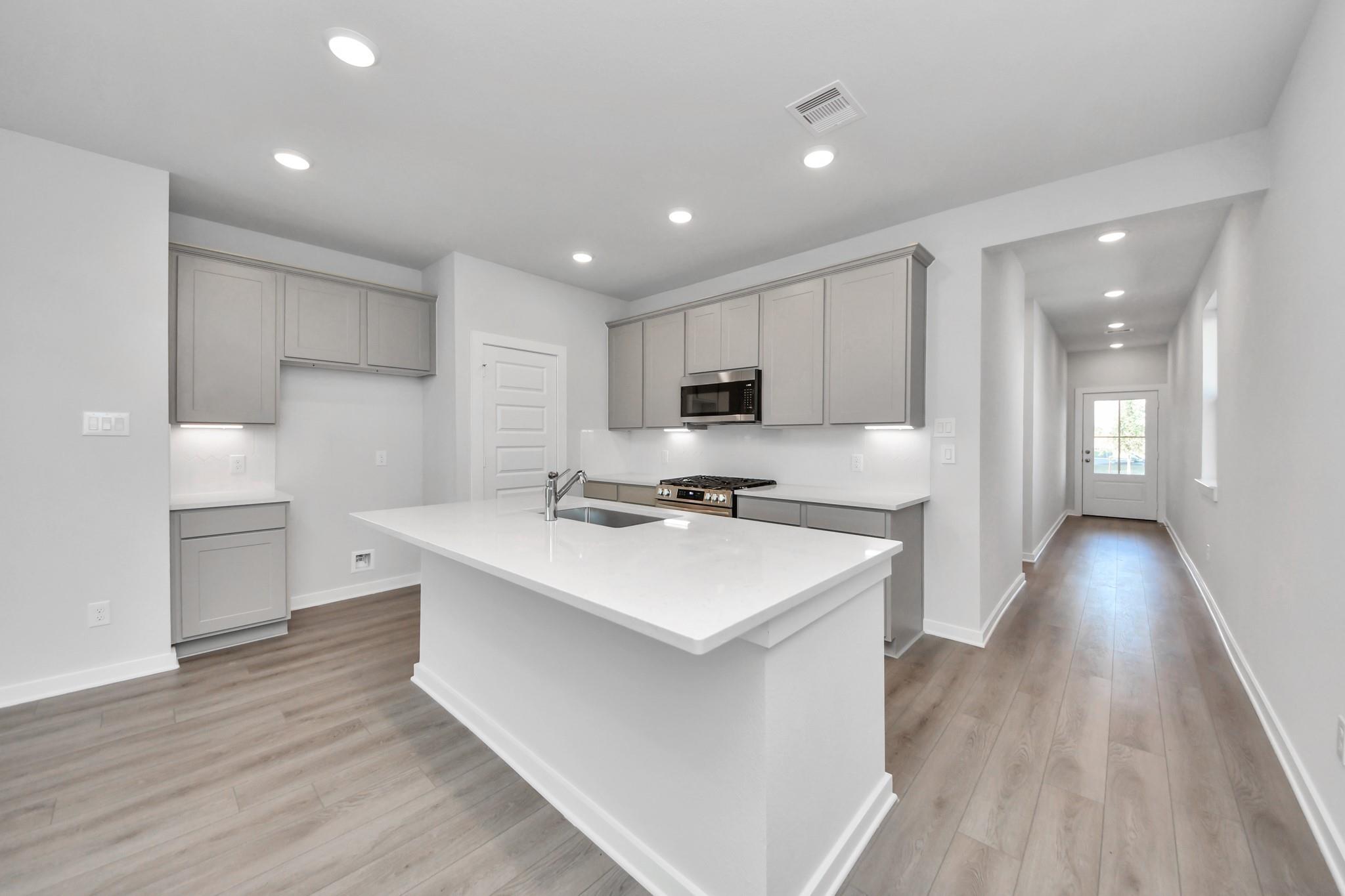 Modern kitchen with white island, gray cabinets, and light wood floors in The Colorado G home at Emberly, Beasley, Texas.