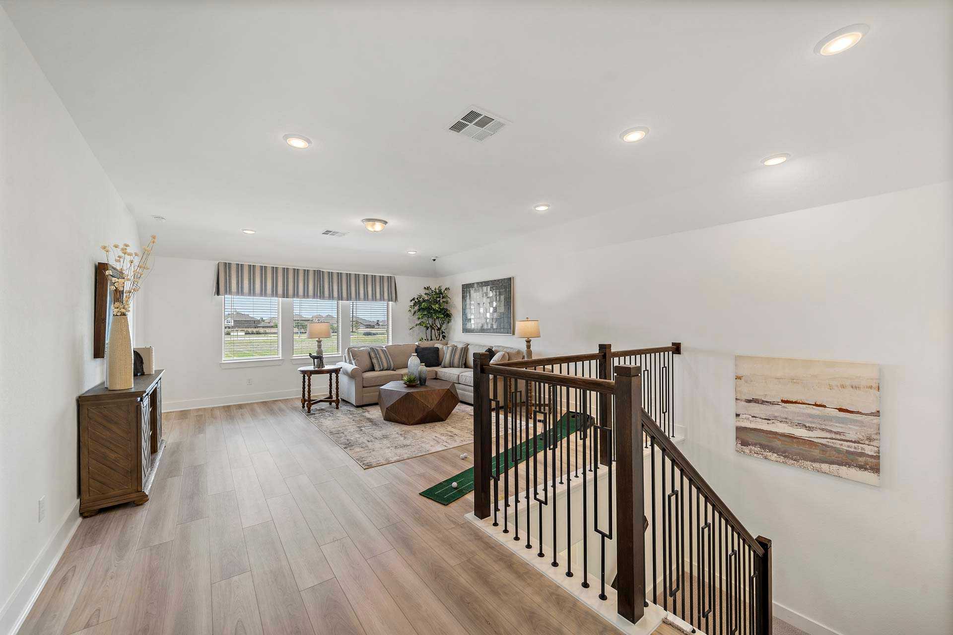 Open-concept living area with staircase in Sierra Vista Rosharon TX by Davidson Homes featuring light wood floors modern decor and large windows