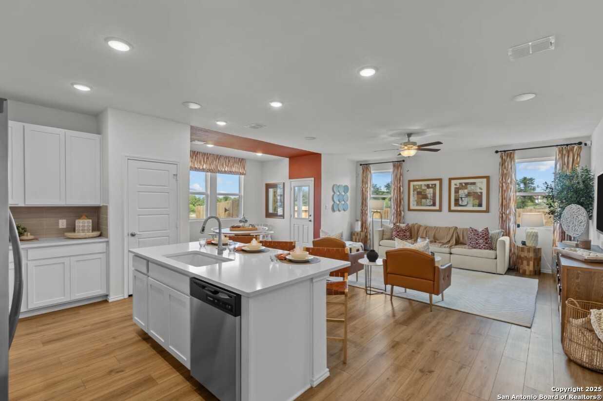 Open-concept kitchen-living area with white island, hardwood floors, and orange sofa in Davidson Homes The Daphne I, Bricewood, San Antonio