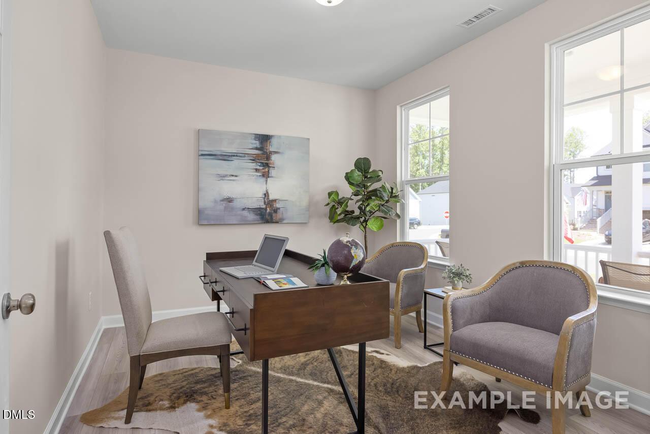 Cozy home office with wooden desk, laptop, abstract wall art, potted fiddle leaf fig, and armchairs in Davidson Homes The Chestnut B, Lillington, NC