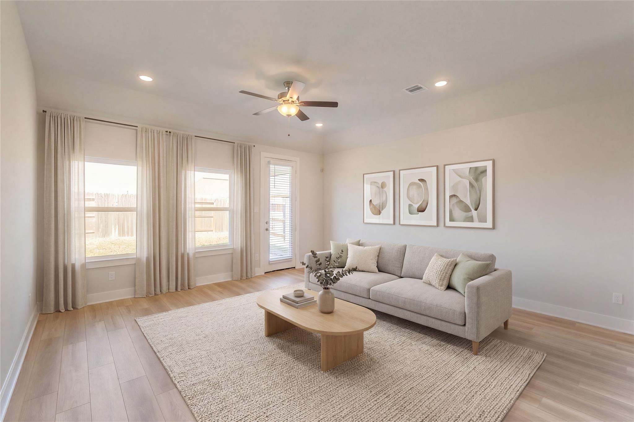 Bright living room with sheer-curtained windows, French doors to backyard, gray sofa, oak coffee table, and ceiling fan in Davidson Homes The Luna L, Sunterra, Katy, Texas