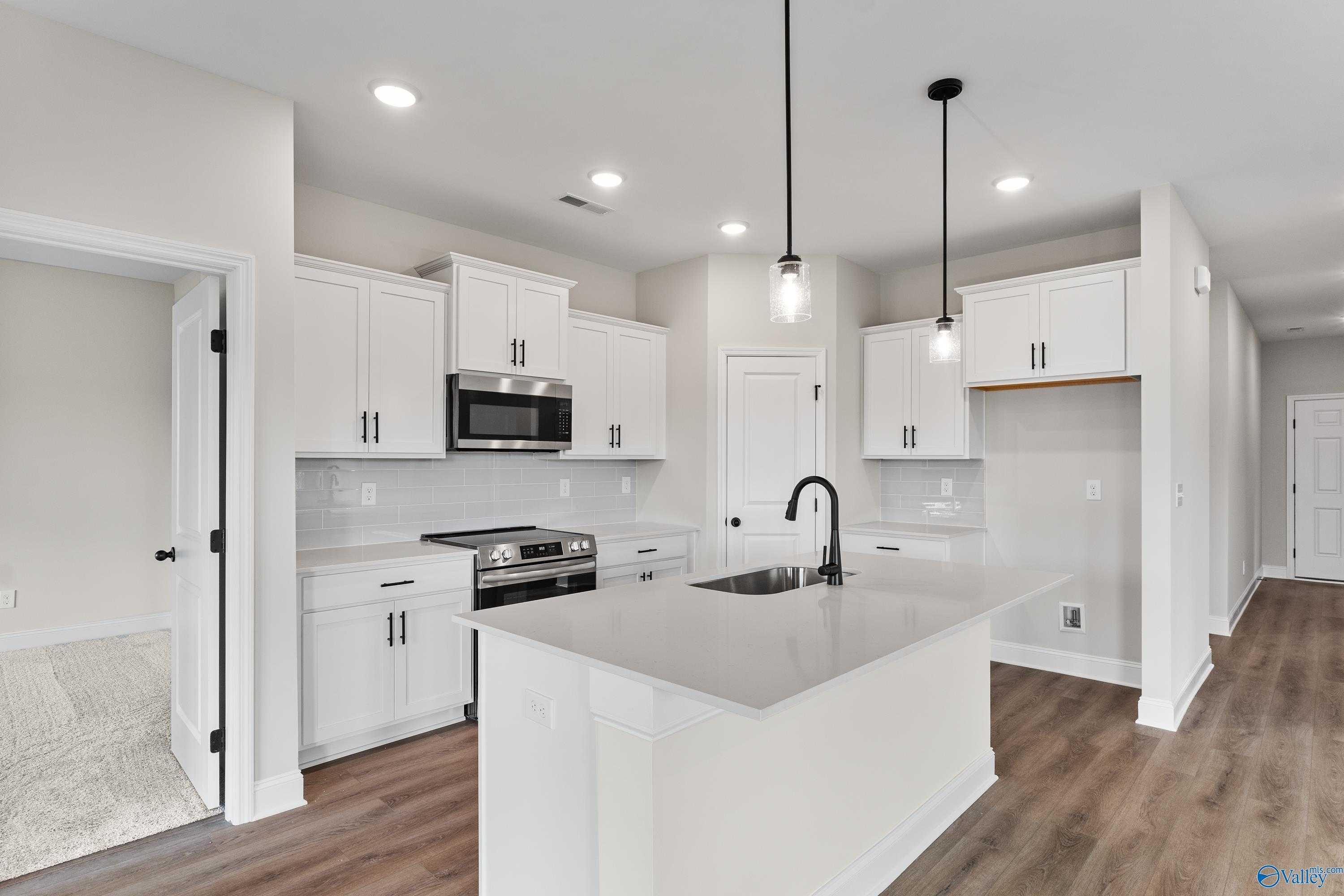 Modern white kitchen with quartz island, stainless appliances, and open layout in Davidson Homes The Franklin B, Hazel Green, AL