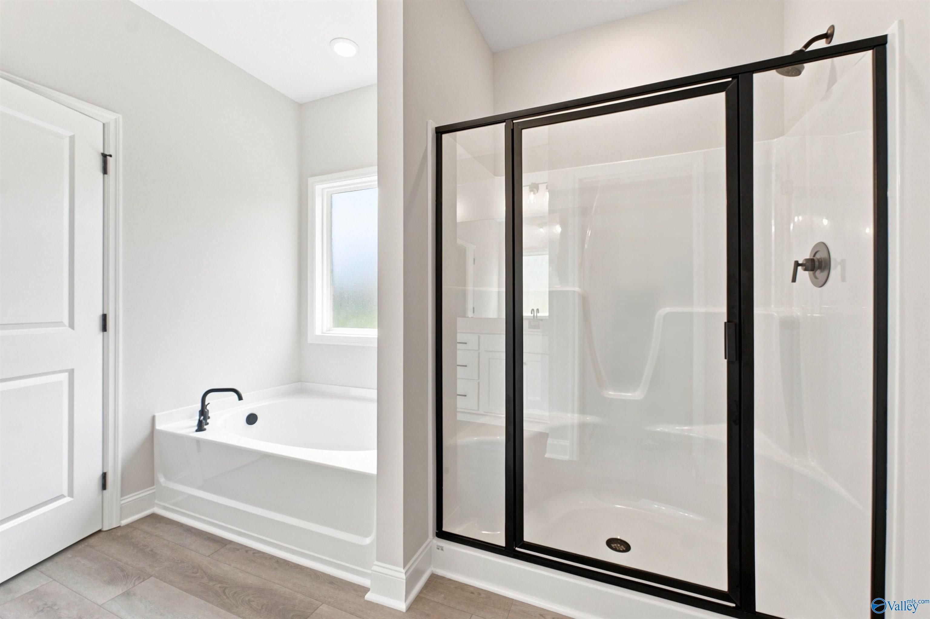 Primary bathroom with garden tub, black-framed glass shower, and vinyl plank flooring in The Everett B, Toney, Alabama