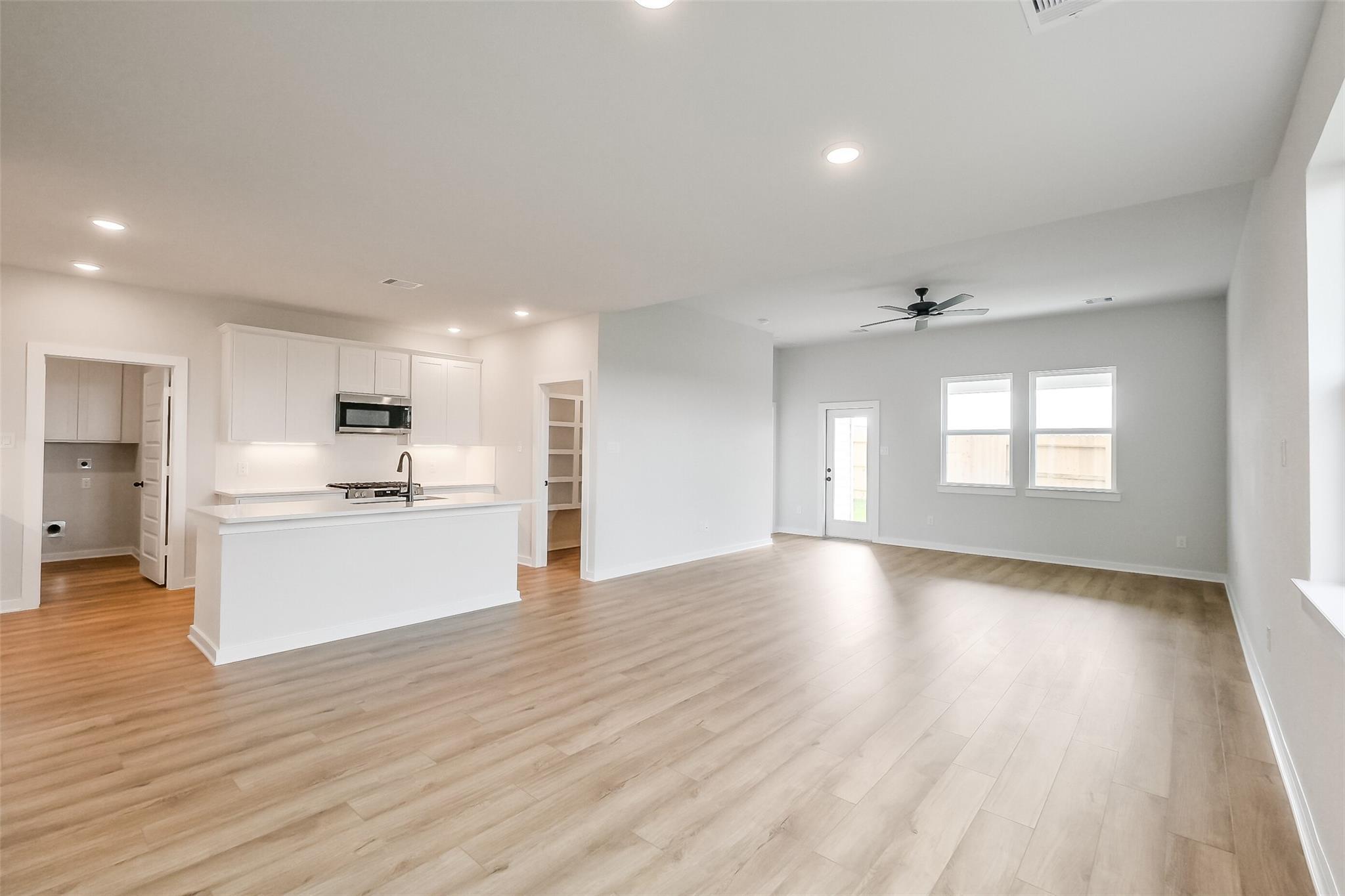Open-concept kitchen-living area with white shaker cabinets, island sink, hardwood floors, and ceiling fan in Davidson Homes Tierra B, Beasley, TX