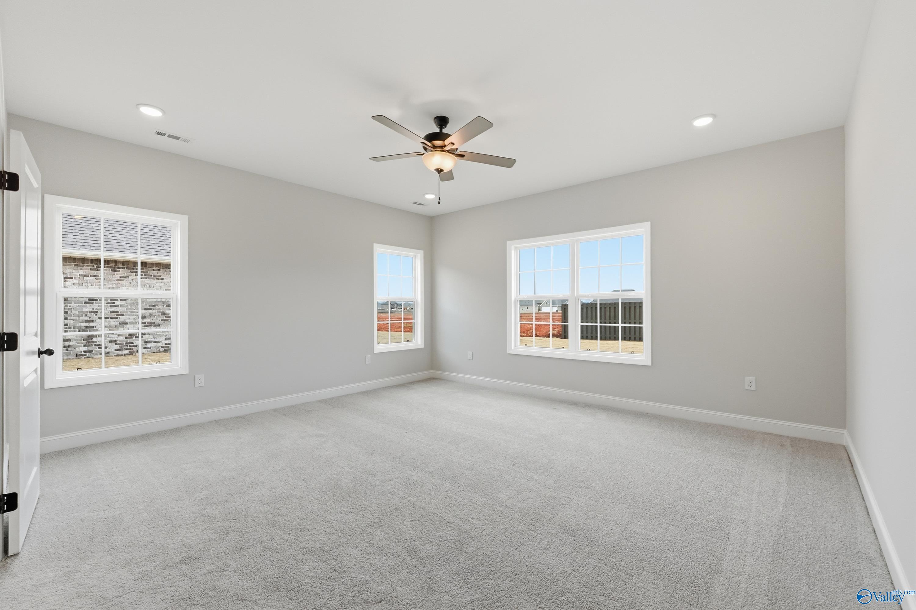 Spacious empty bedroom with light gray walls, ceiling fan, and large windows in Davidson Homes The Finleigh, Meridianville, Alabama