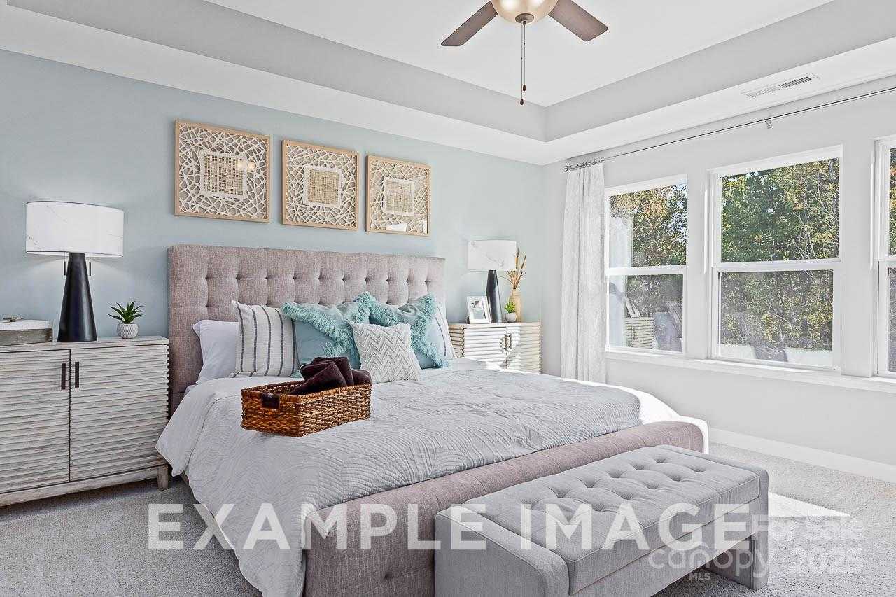 Elegant master bedroom with tufted headboard, ceiling fan, and tree-view windows in Davidson Homes The Hemlock A, Belmont, NC