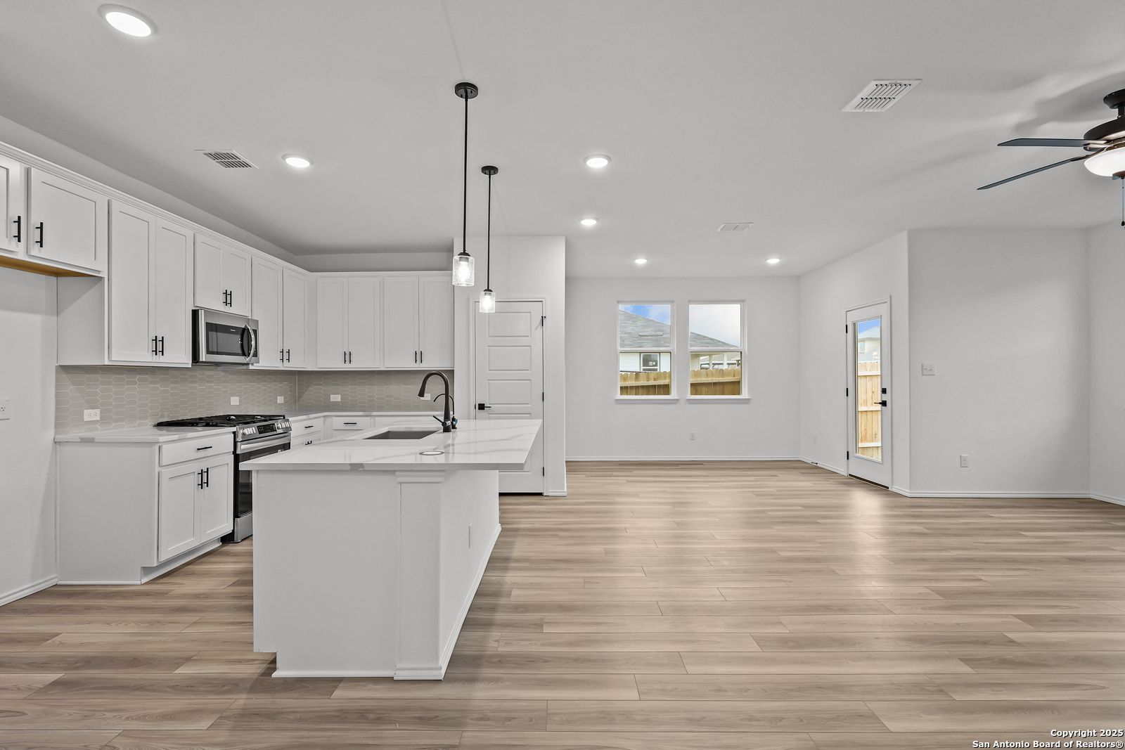 Modern white kitchen with quartz island, stainless appliances, pendant lights in open-concept The Daphne J by Davidson Homes, Converse TX