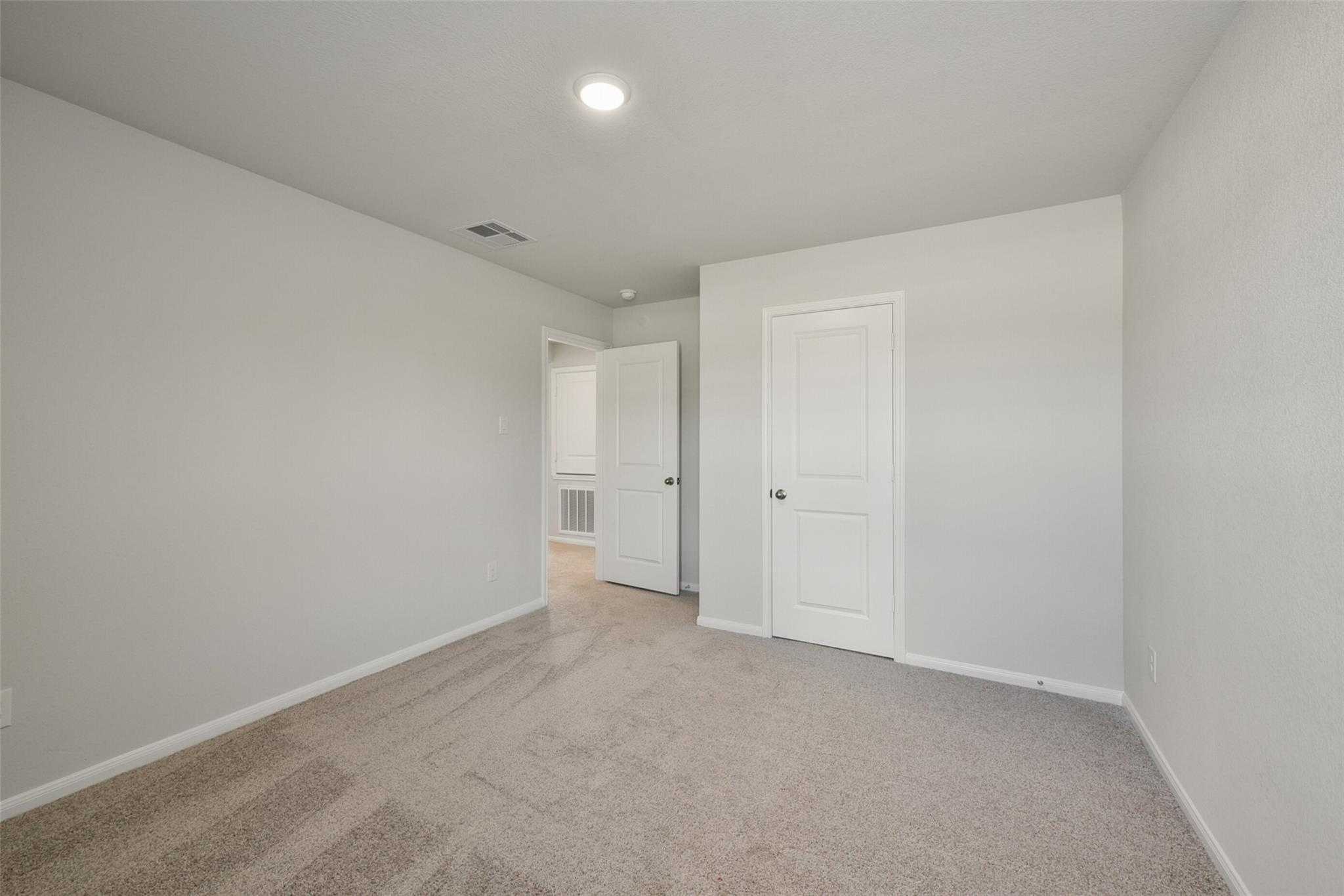 Bright secondary bedroom with light gray walls, beige carpet, and hallway access in The Sabine E by Davidson Homes, Dayton, Texas