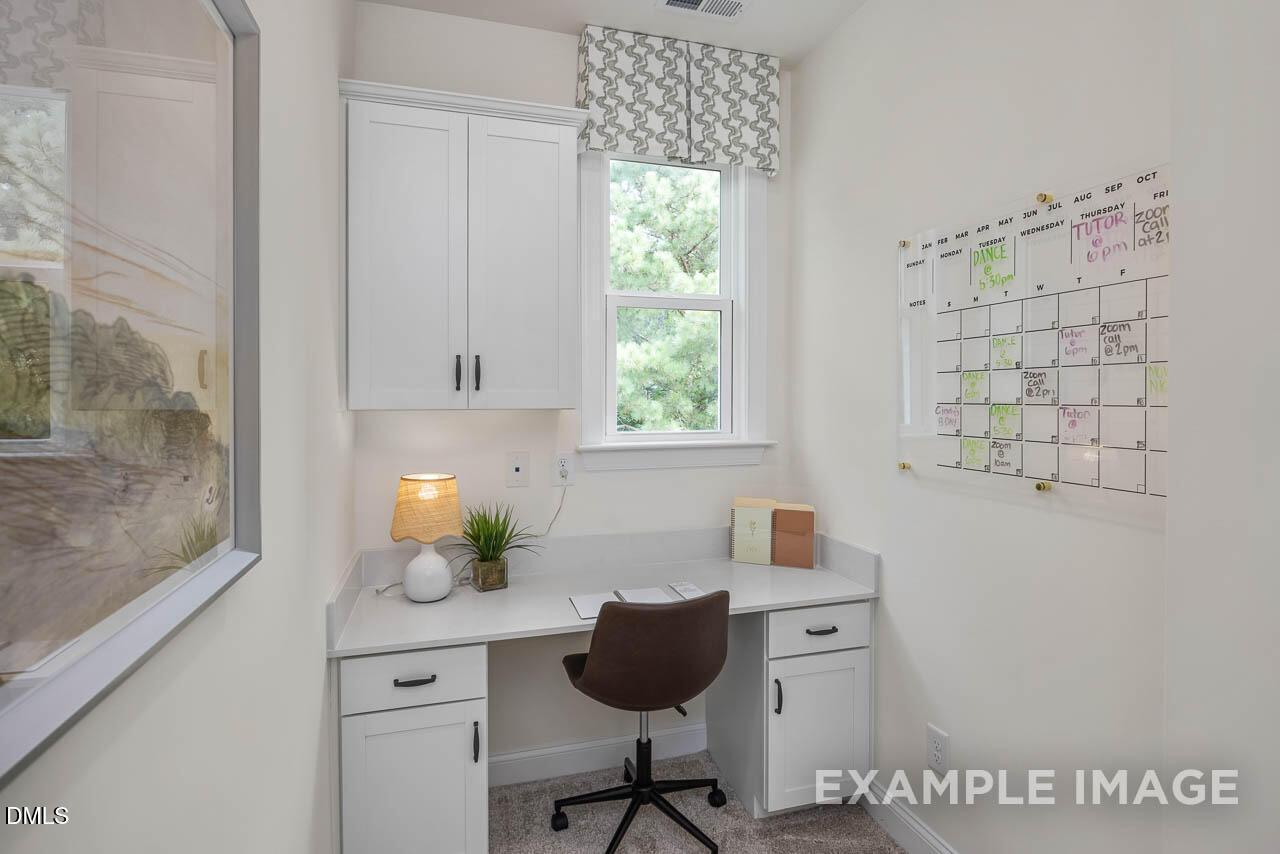 Bright home office with white built-in cabinets, wooden desk, leather chair, and window view in 4-bedroom Davidson Homes The Crawford D, Angier, NC