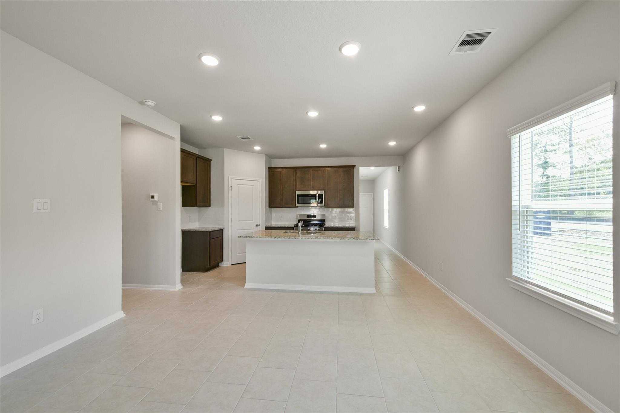 Open kitchen with white island, wooden cabinets, and stainless sink in airy living space, The Sabine E by Davidson Homes, Dayton, TX