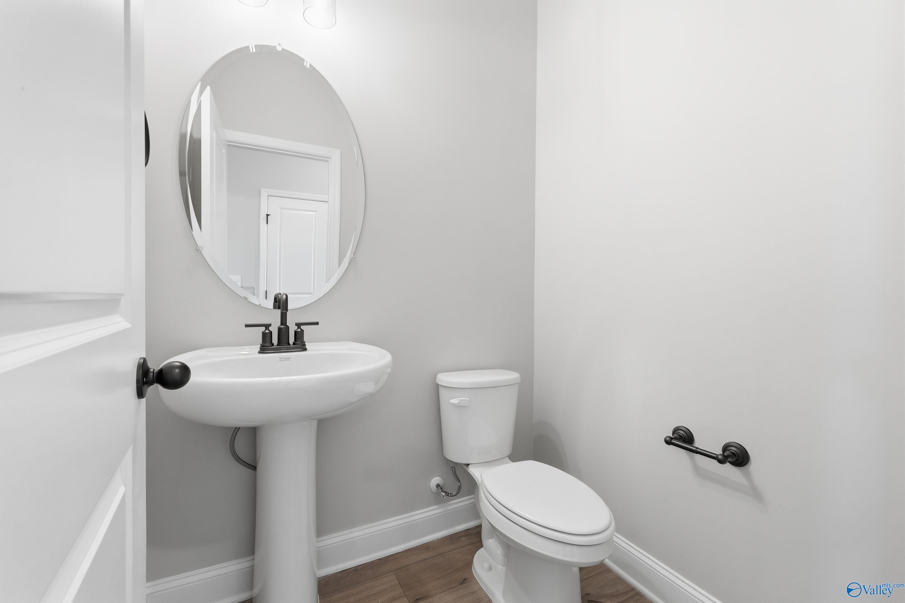 Elegant powder room featuring pedestal sink, oval mirror, and toilet in Davidson Homes The Rockford, Creekside, Harvest, Alabama