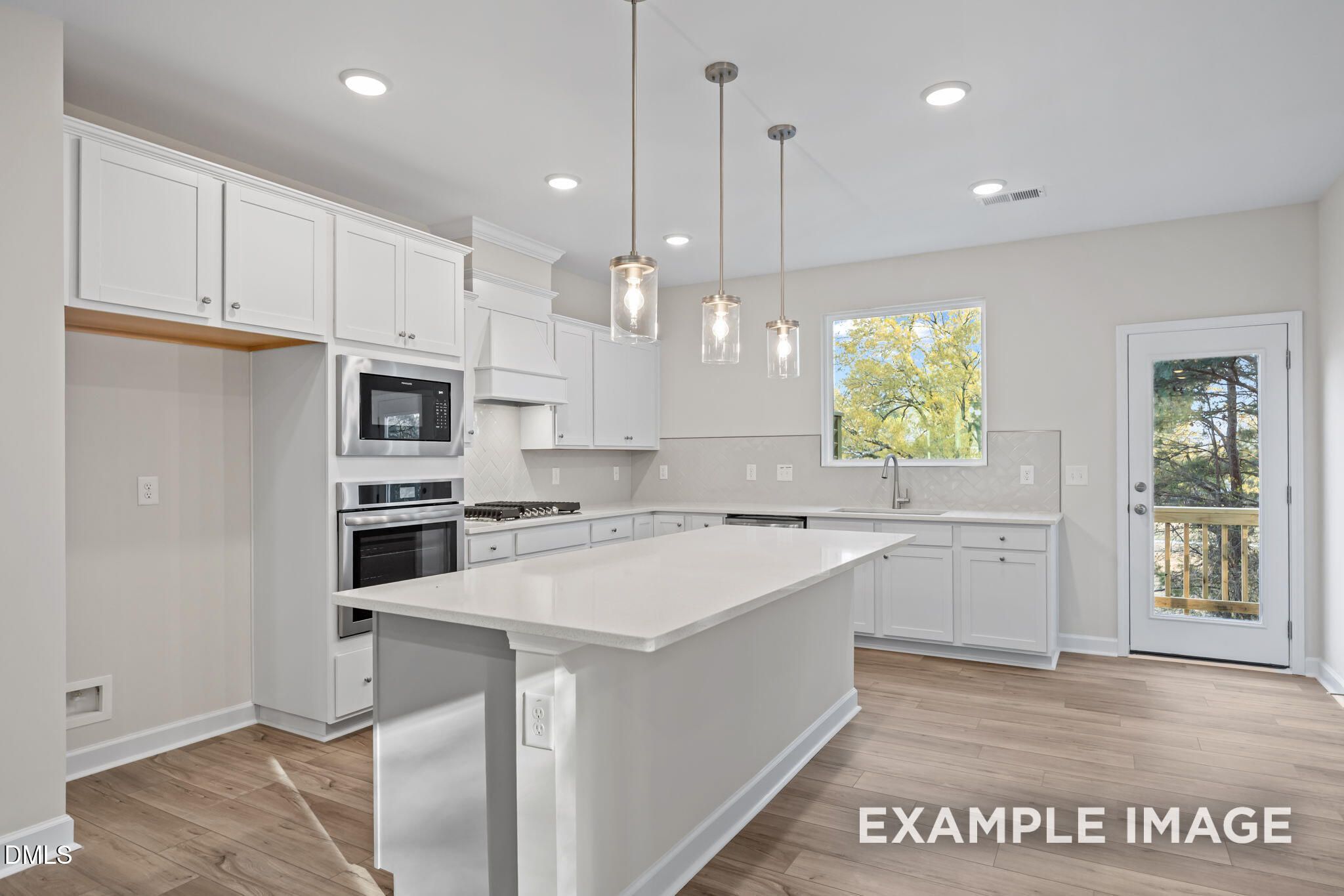 Modern white kitchen with quartz island, stainless steel appliances, pendant lights, and deck view in Davidson Homes The Avery, Knightdale, NC