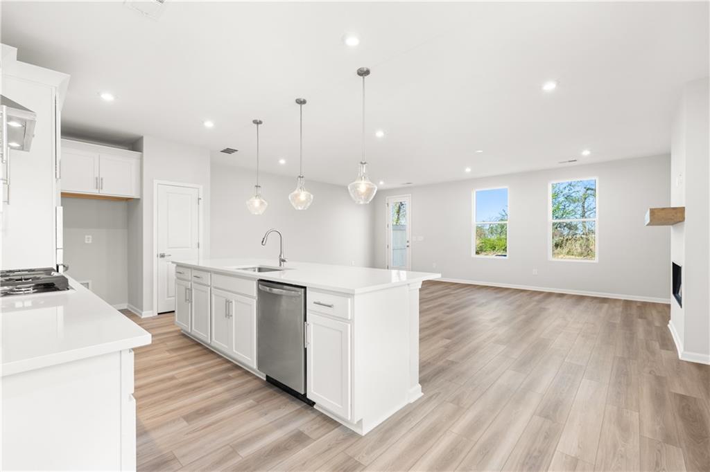 Modern white kitchen with quartz island, stainless dishwasher, gas range, and open living area in Davidson Homes The Cary A, Winder, GA