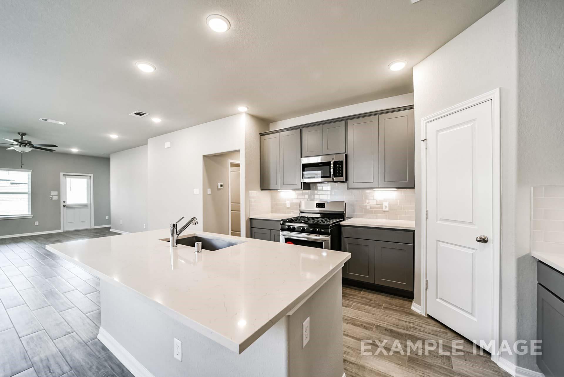 Modern kitchen with gray cabinets, quartz island, and stainless appliances in The Riviera A plan at Emberly, Beasley, TX.