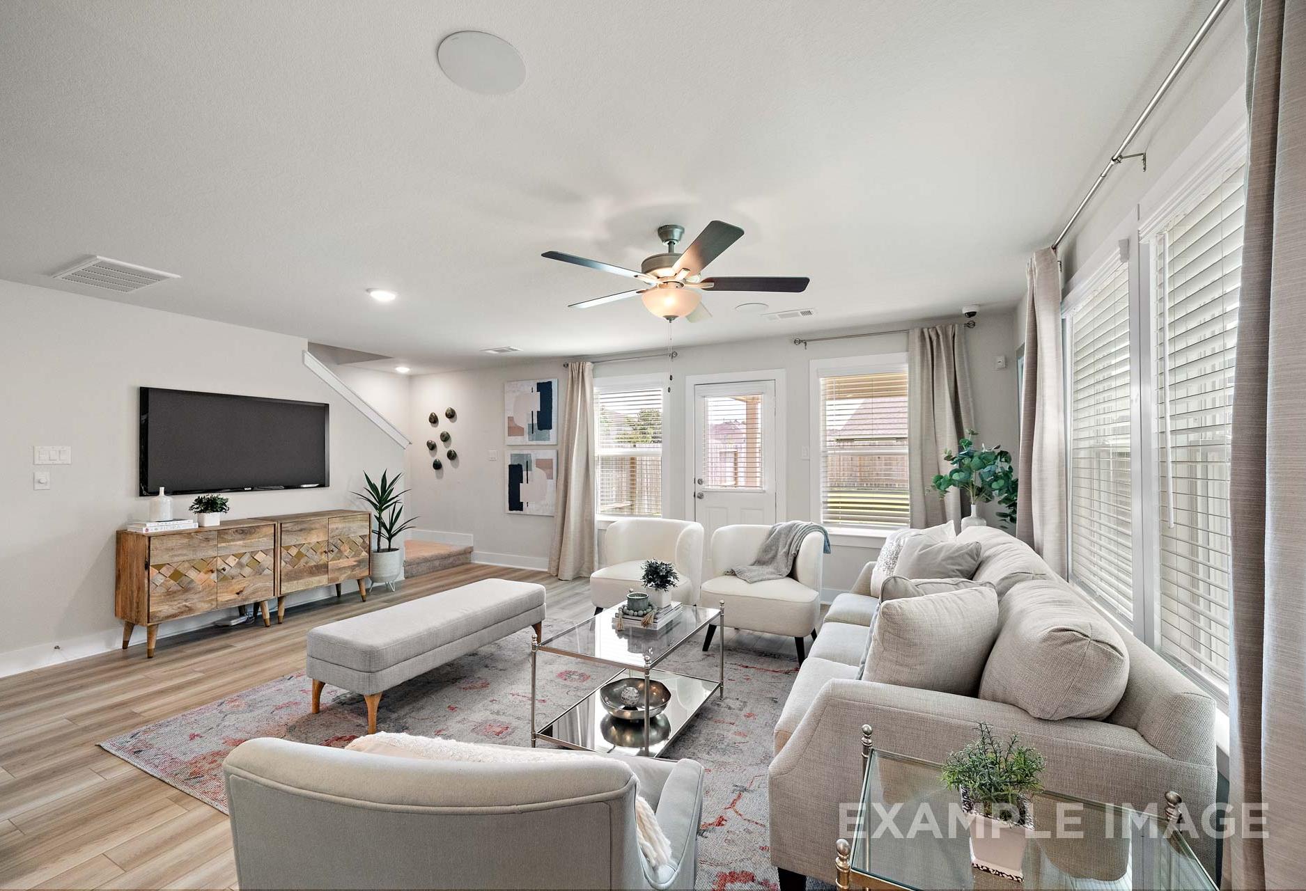 Spacious living room in The Lily A by Davidson Homes, featuring beige sectional sofa, wooden TV stand, large windows, and ceiling fan