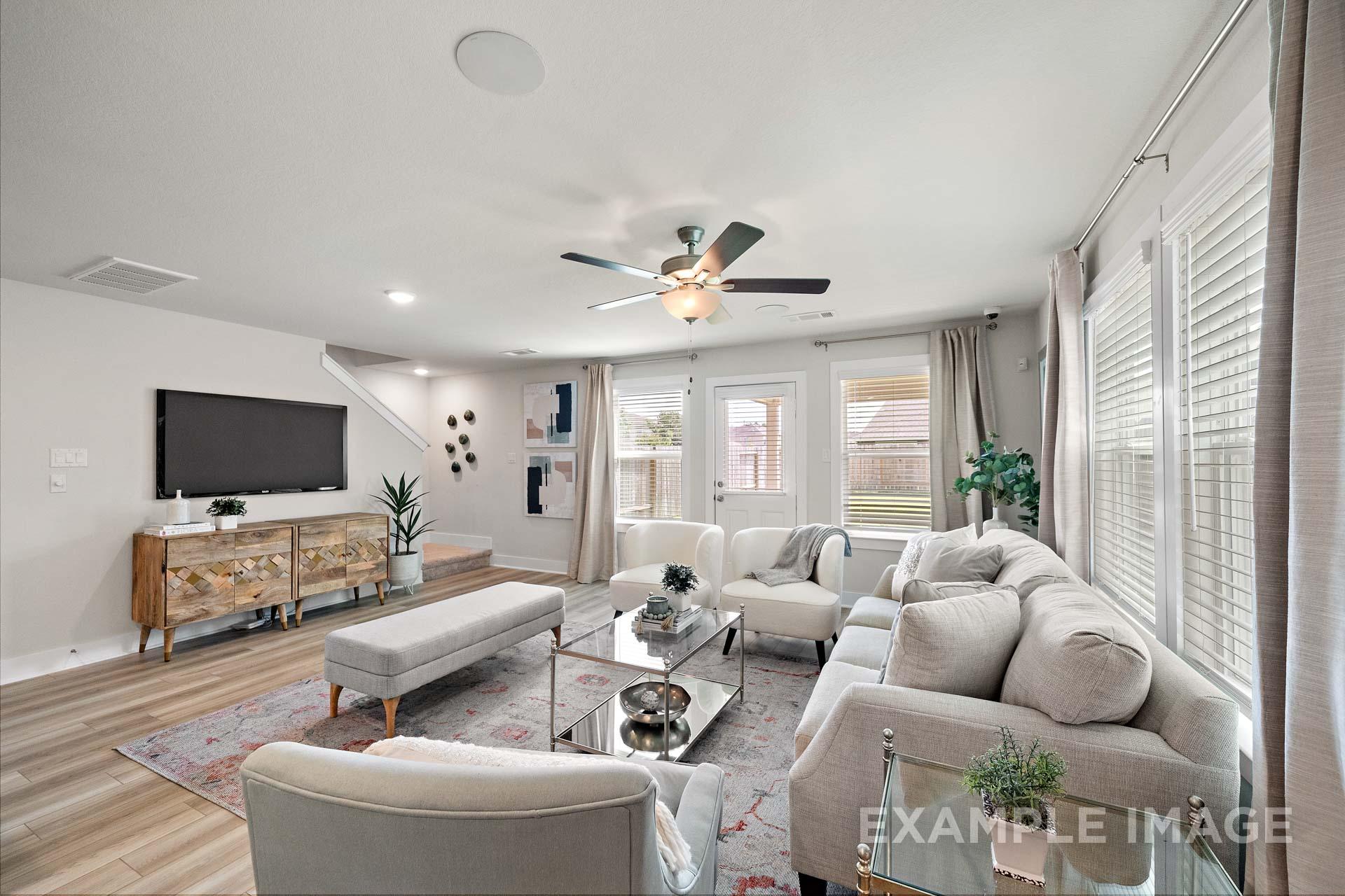 Spacious living room in The Lily A by Davidson Homes, featuring beige sectional sofa, wooden TV stand, large windows, and ceiling fan