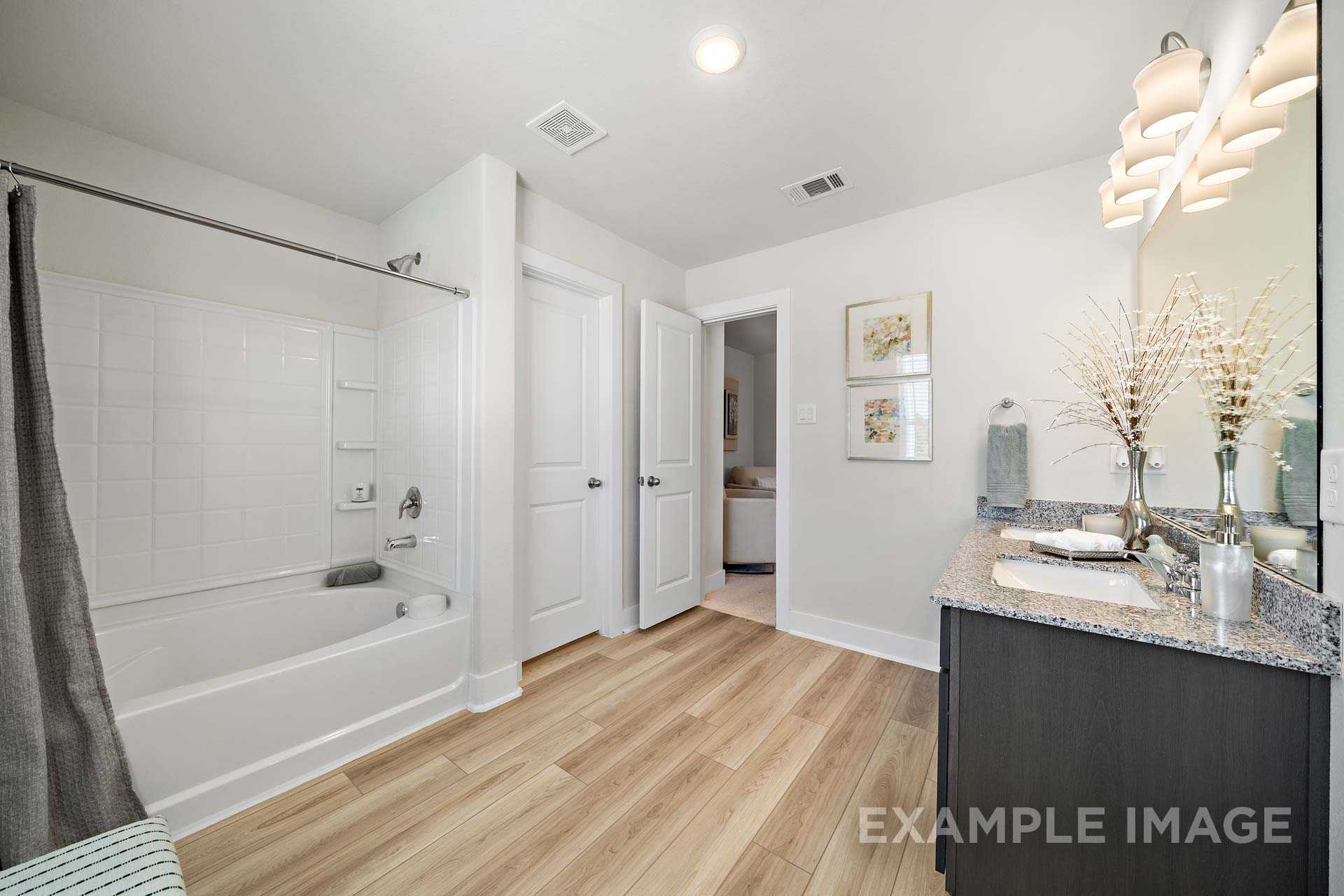 Spacious master bath in The Lily A featuring walk-in shower, freestanding tub, double vanity with quartz counters, and hardwood floors