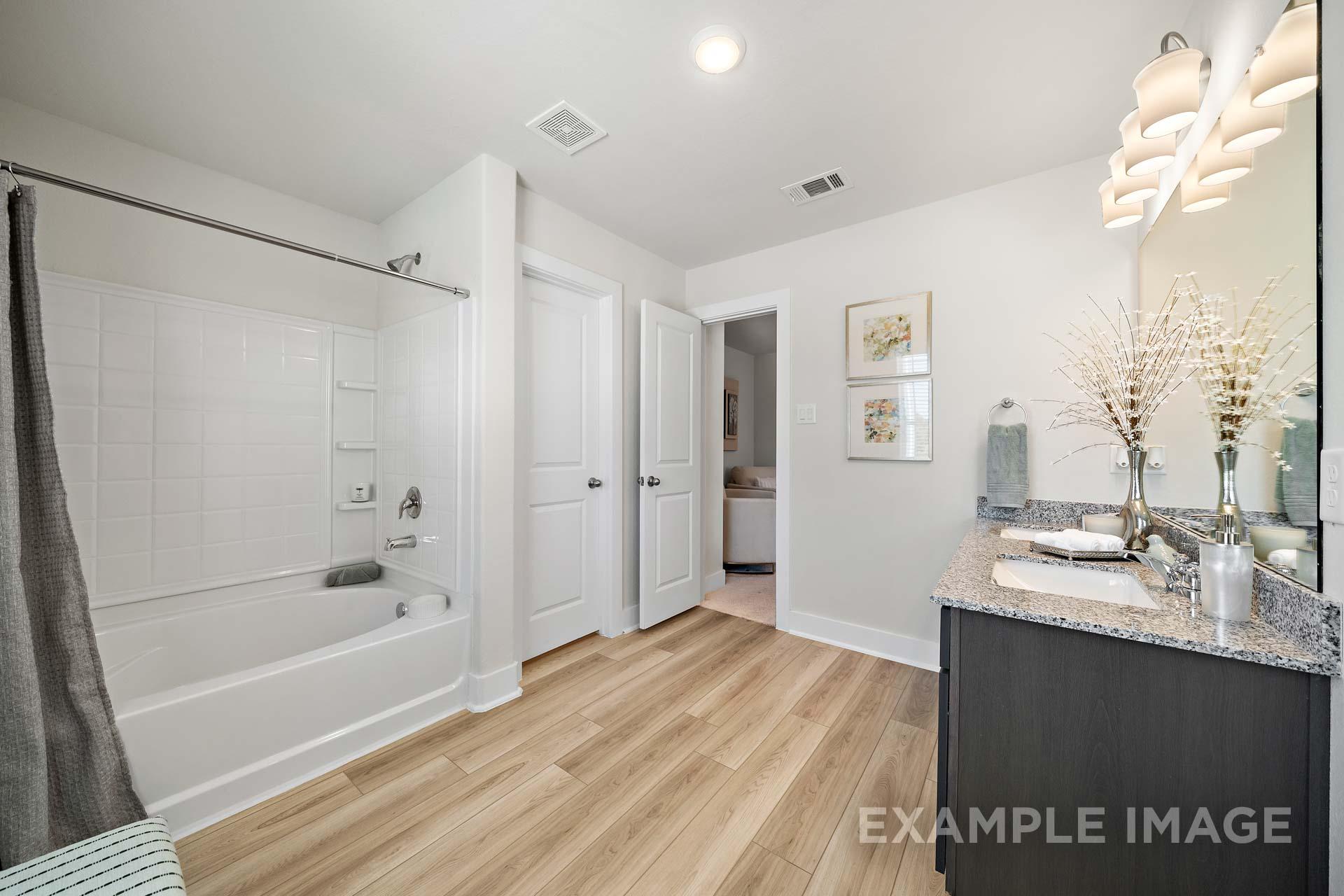 Spacious master bath in The Lily A featuring walk-in shower, freestanding tub, double vanity with quartz counters, and hardwood floors
