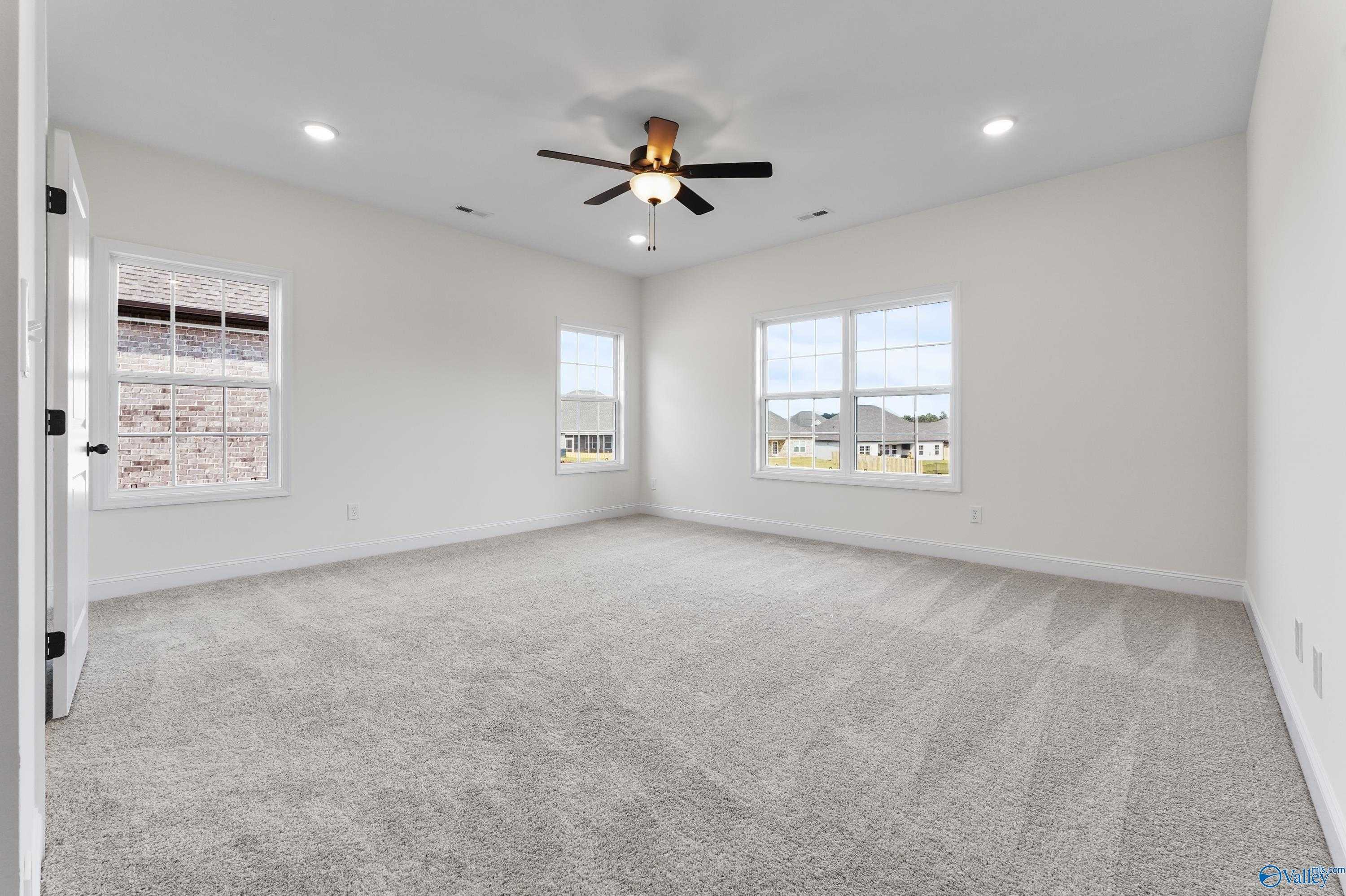 Bright empty bedroom with ceiling fan, large windows, and neutral carpet in The Finleigh 3-bedroom home by Davidson Homes, Harvest AL