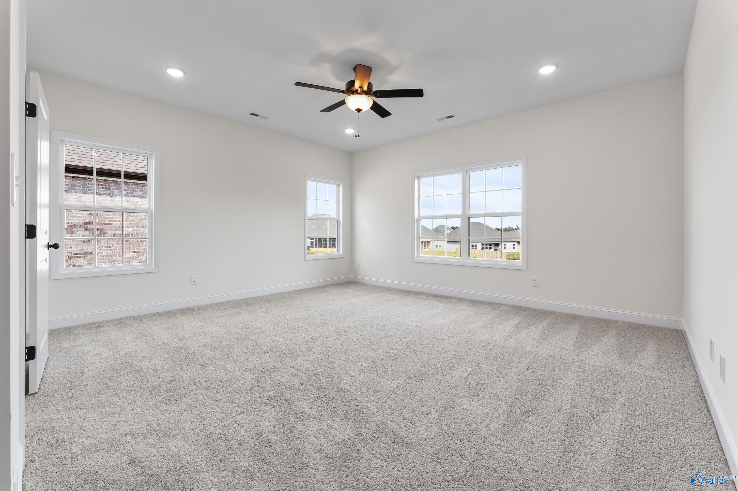 Bright empty bedroom with ceiling fan, large windows, and neutral carpet in The Finleigh 3-bedroom home by Davidson Homes, Harvest AL