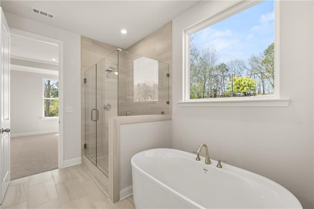Luxurious master bathroom with freestanding tub, glass shower enclosure, and wooded window view in Davidson Homes Danbury C, Buford GA