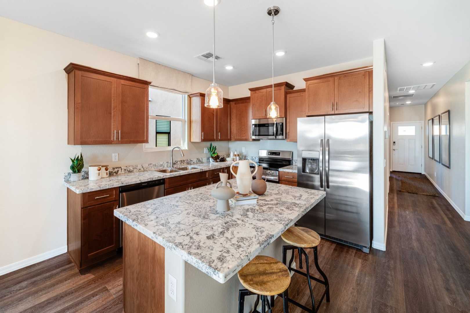 Spacious kitchen in The Savannah C with granite island, wooden cabinets, stainless steel appliances, and bar stools