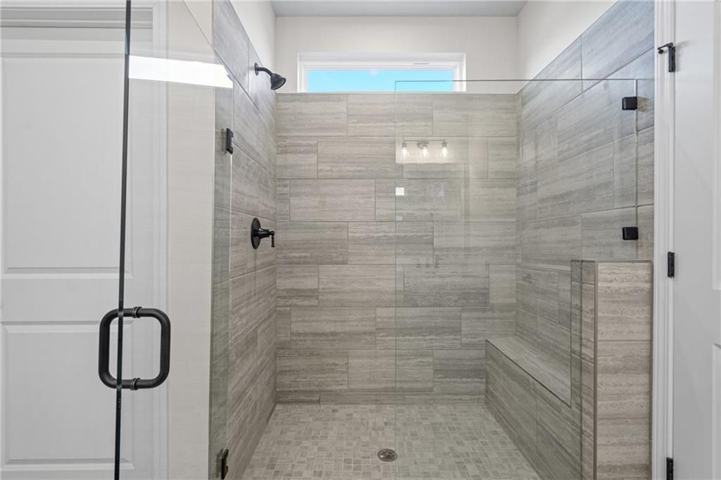 Modern walk-in shower with gray slate tiles, glass enclosure, and bench in master bath of Davidson Homes The Edison B, Loganville, GA