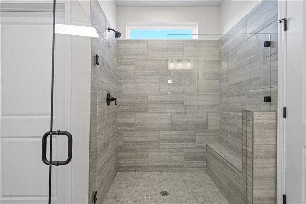 Modern walk-in shower with gray tile walls, frameless glass doors, built-in bench, and window in The Edison B master bath, Loganville, GA