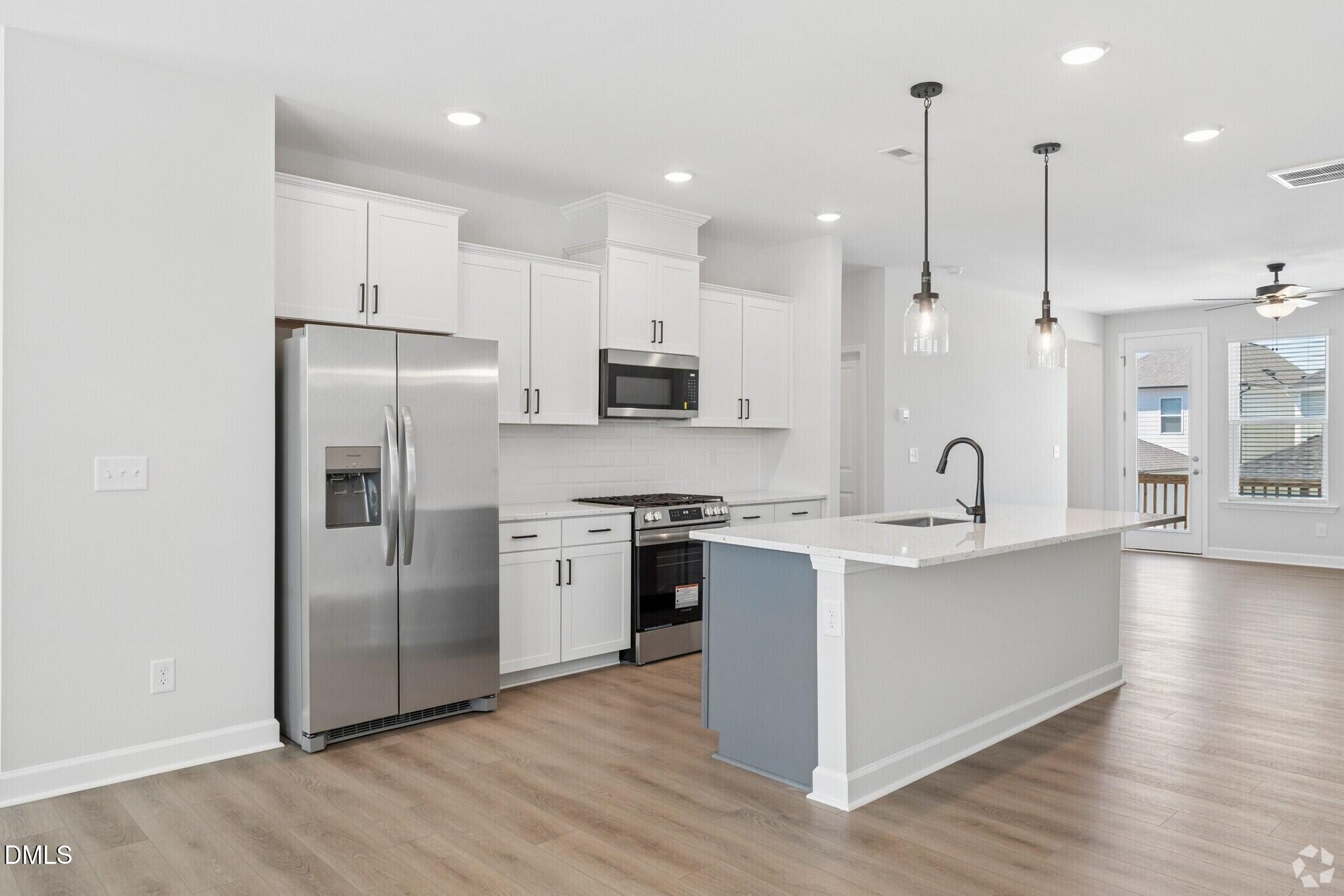 Bright open-concept kitchen with white shaker cabinets, stainless appliances, and large island in Davidson Homes' Mitchell plan, Knightdale NC