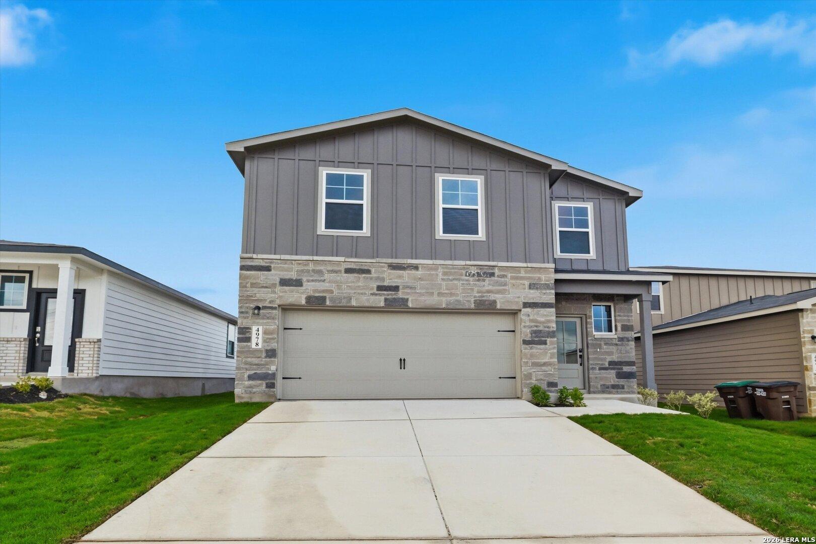 Modern 2-story 4-bedroom home with gray board-and-batten siding, stone accents, 2-car garage, driveway in Agave, San Antonio, Texas