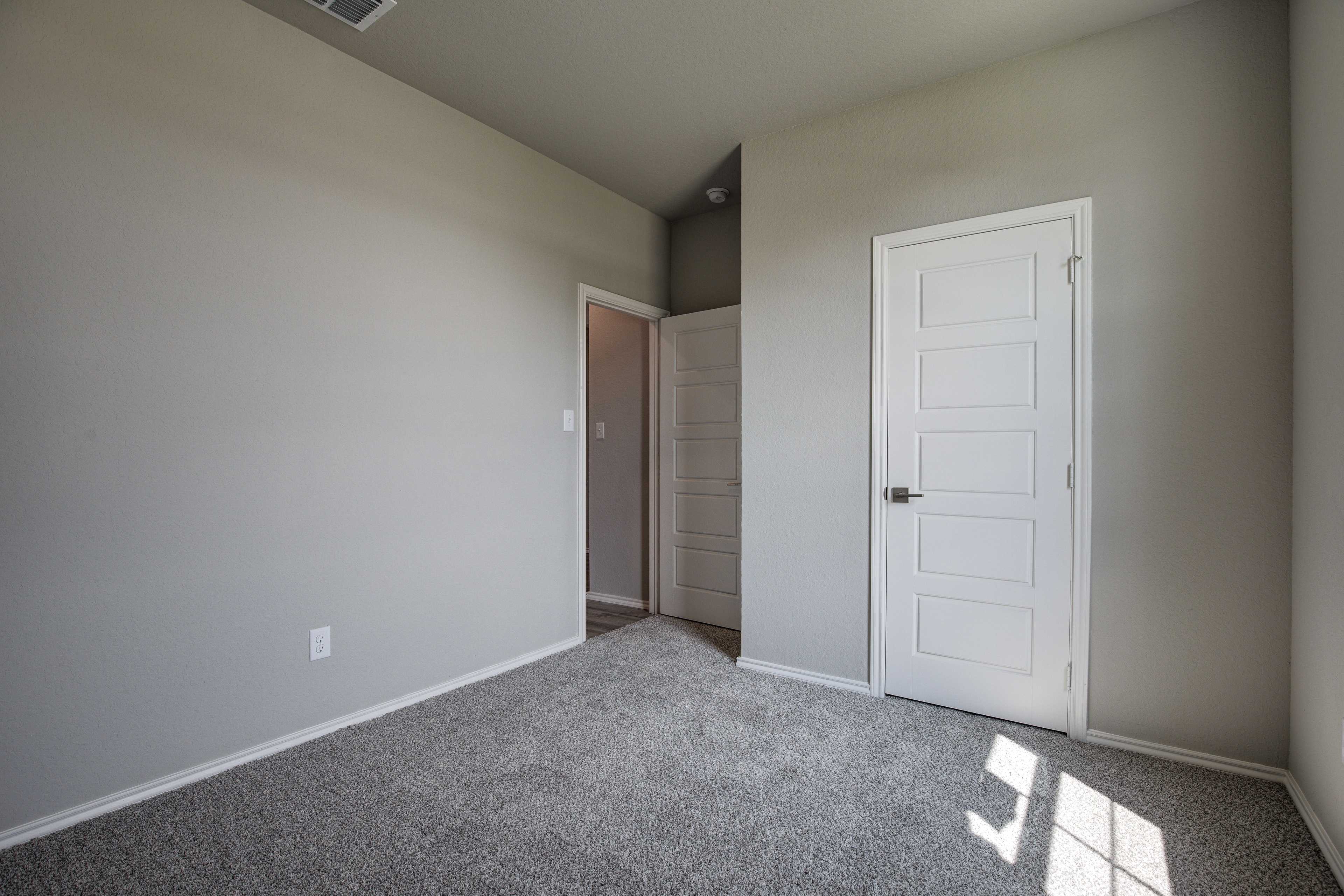 Spacious master bedroom in The Asheville home with neutral beige walls, gray carpet flooring, and white paneled doors