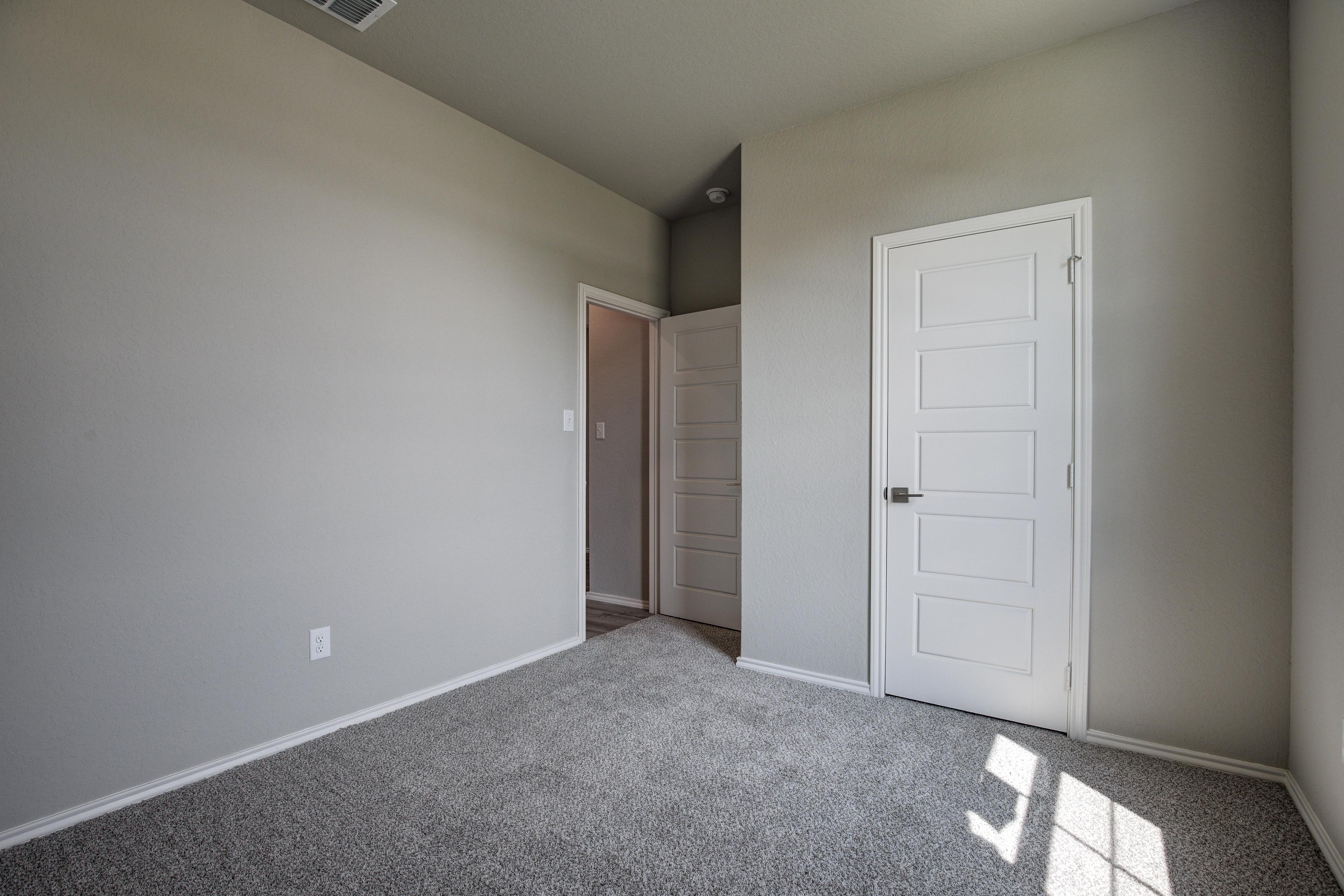 Spacious master bedroom interior in The Asheville home design featuring light gray walls, plush carpet, and white paneled doors
