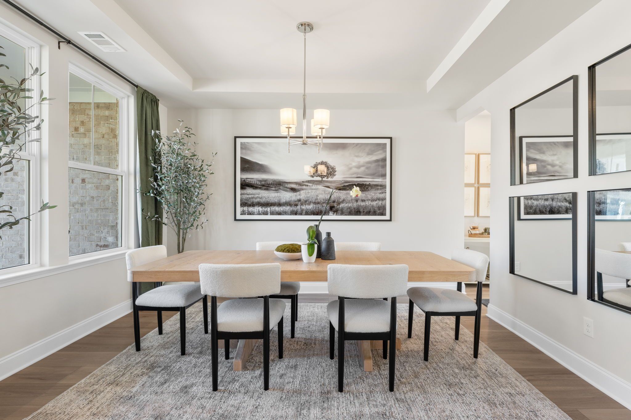 Elegant dining room at Melody Lakeside Estates in Buford Georgia with rectangular wood table, white chairs, chandelier, and large black-and-white art
