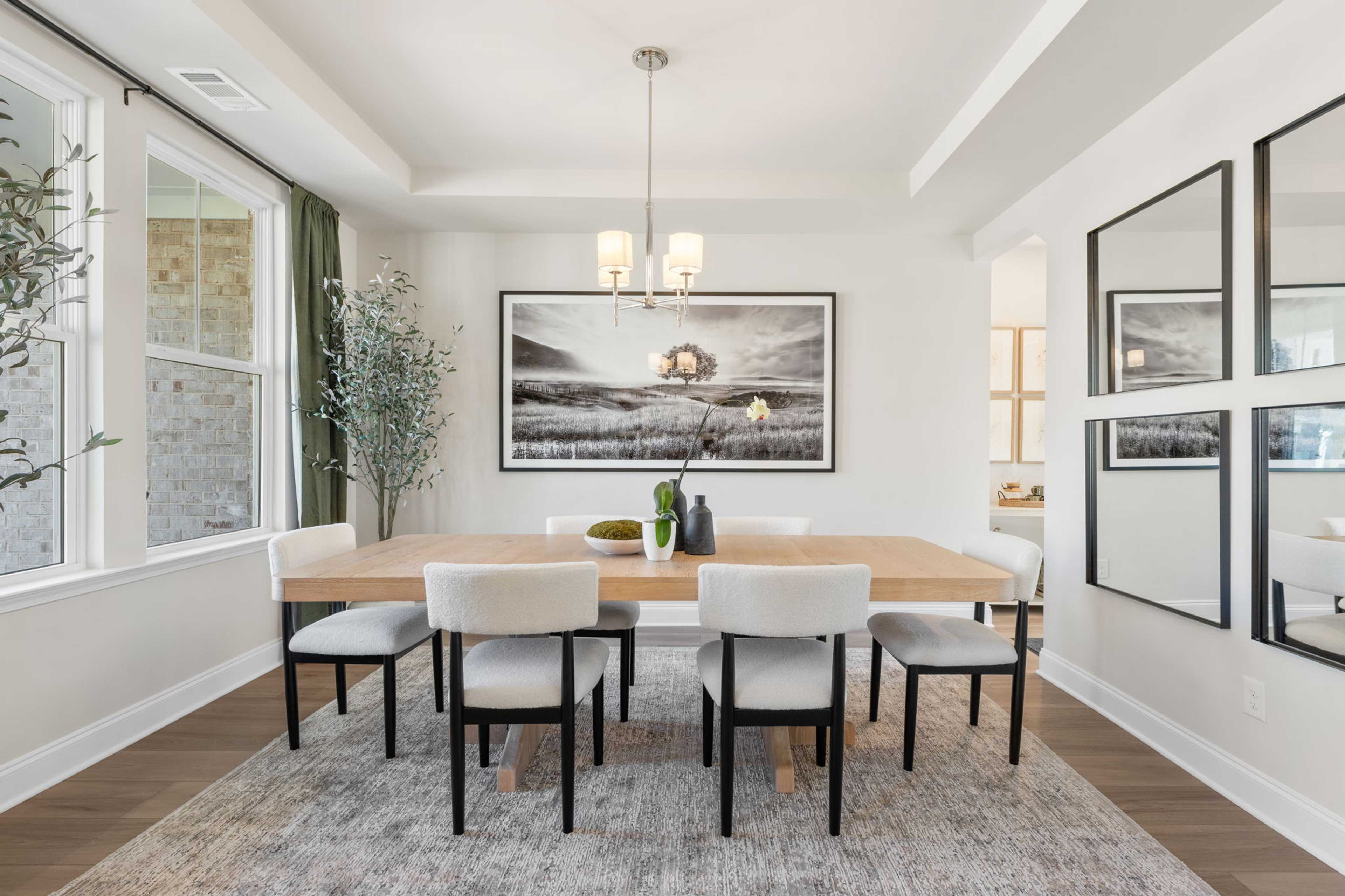 Elegant dining room at Melody Lakeside Estates in Buford Georgia with rectangular wood table, white chairs, chandelier, and large black-and-white art