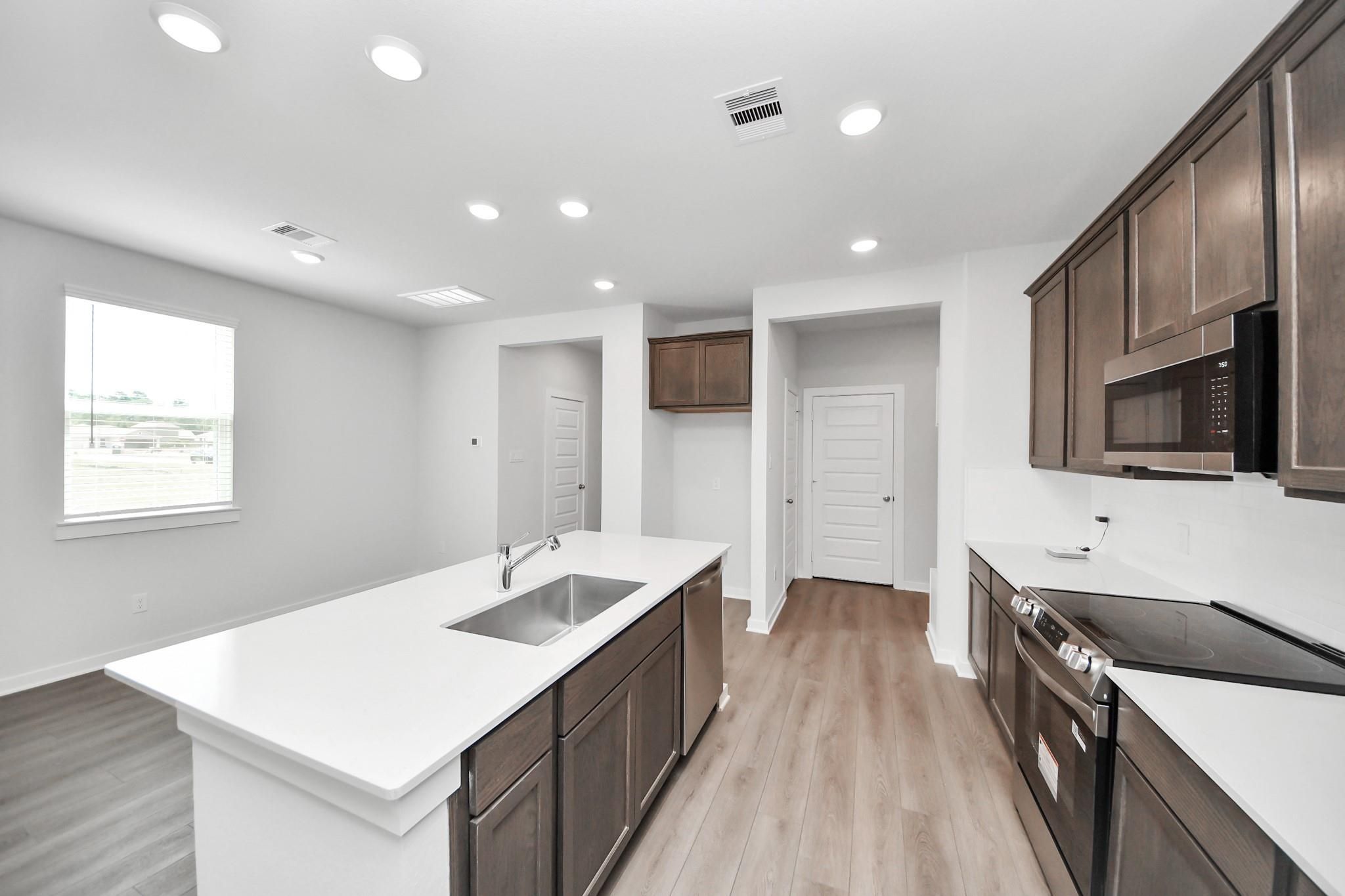 Modern kitchen with white countertops and dark wood cabinets in The Brazos F floor plan at Liberty Estates, Cleveland, TX.