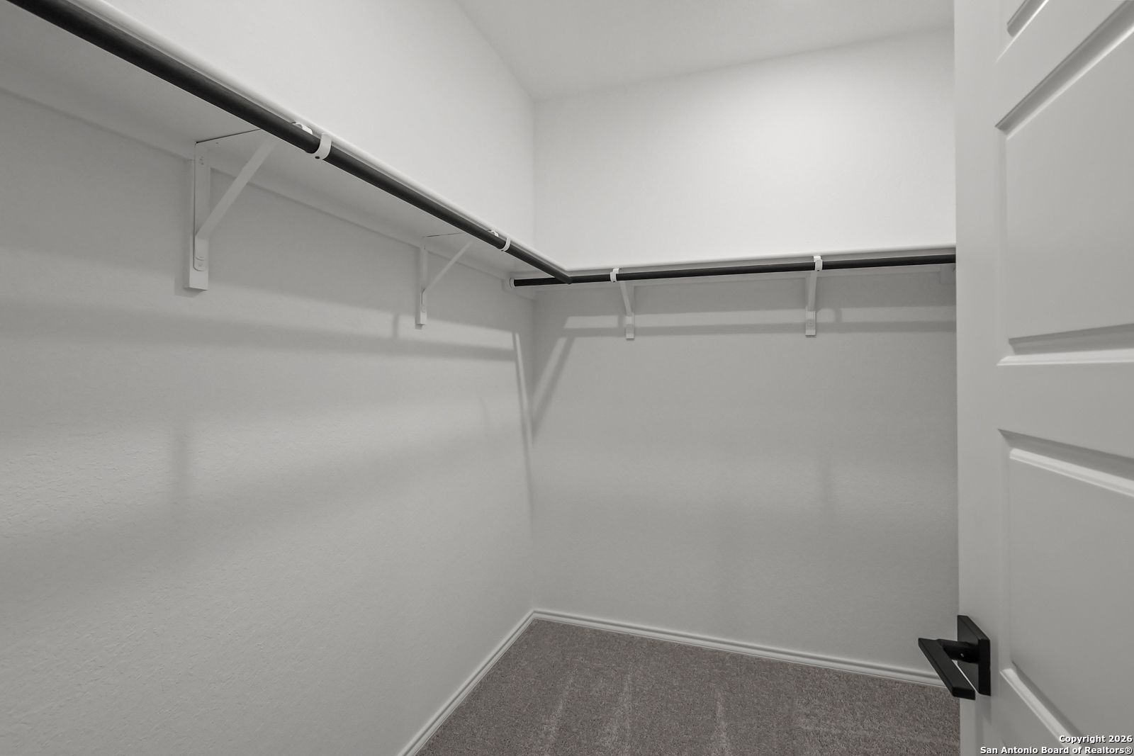 Spacious walk-in closet with white walls, hanging rods and carpeted floor in Davidson Homes The Douglas E, San Antonio, Texas