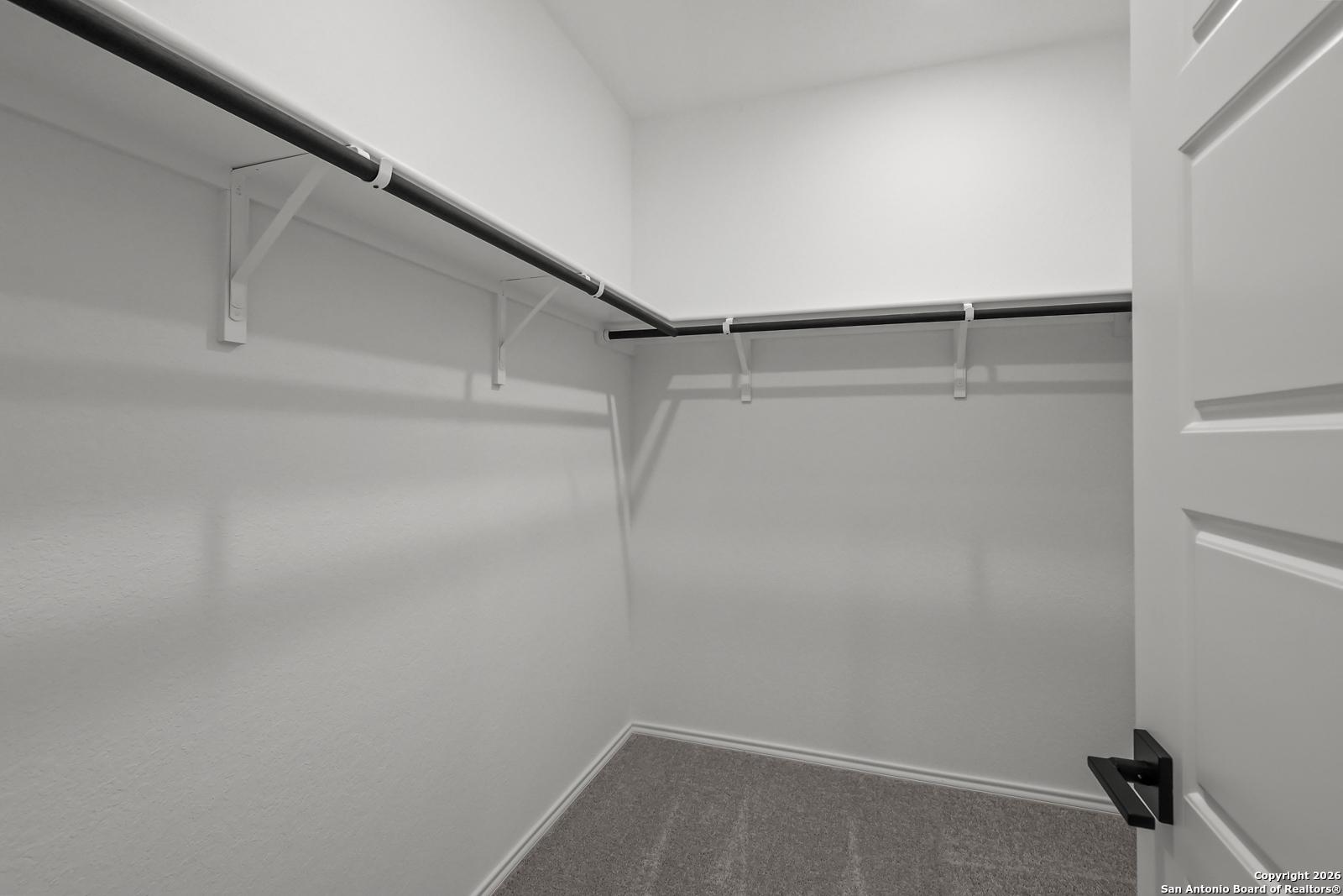 Spacious walk-in closet with white walls, hanging rods and carpeted floor in Davidson Homes The Douglas E, San Antonio, Texas