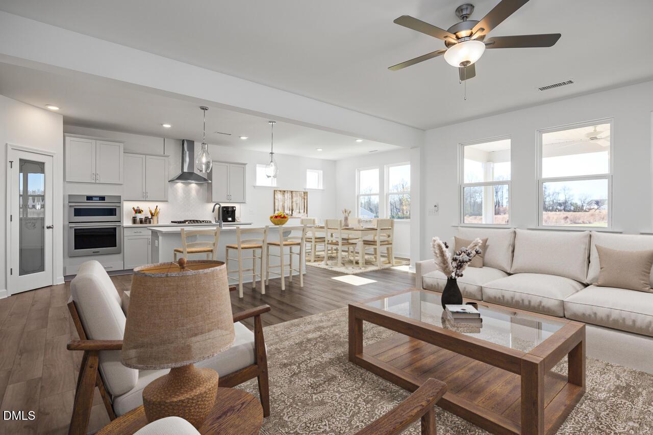 Open-concept kitchen and living room with white cabinets, stainless appliances, island bar, and beige sofa in Davidson Homes The Cypress B II, Angier, NC