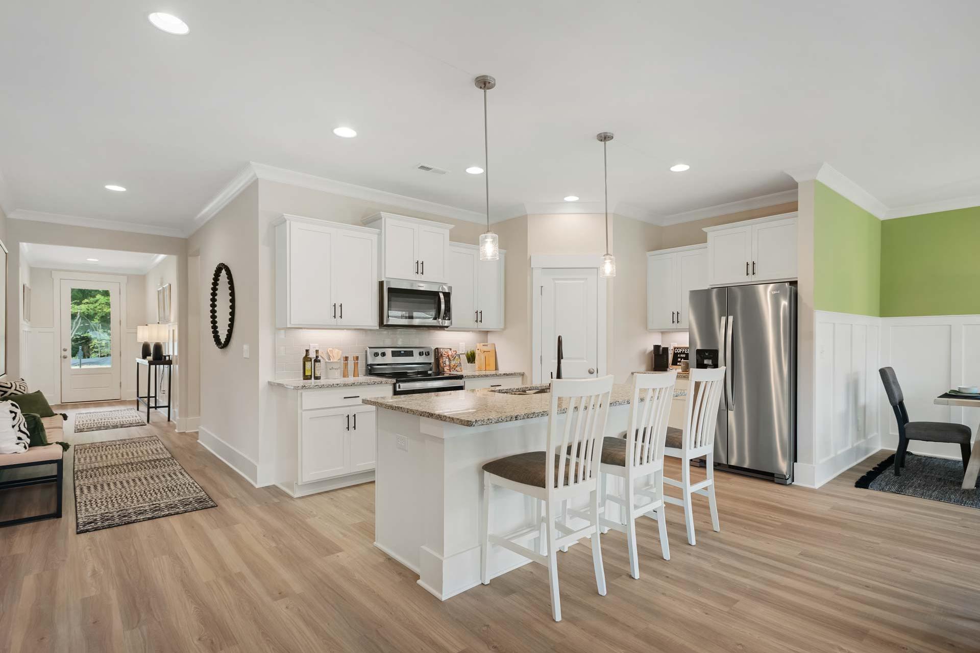 Spacious open-concept kitchen at Durham Farms in Harvest Alabama with white cabinets, center island, stainless appliances, and hardwood floors