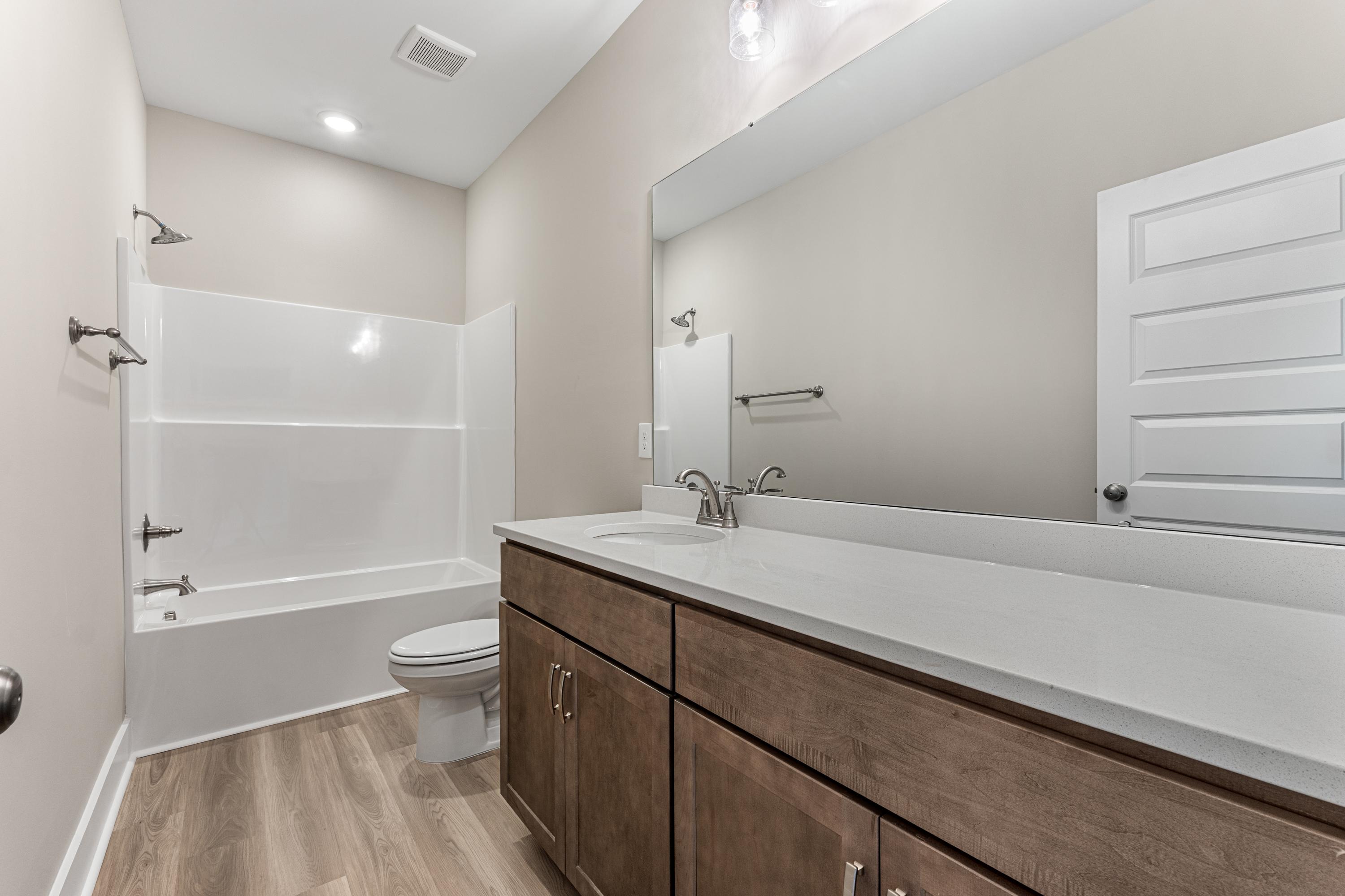 Spacious bathroom in The Oxford C with white tiled tub-shower combo, quartz vanity, toilet, and wood-look flooring