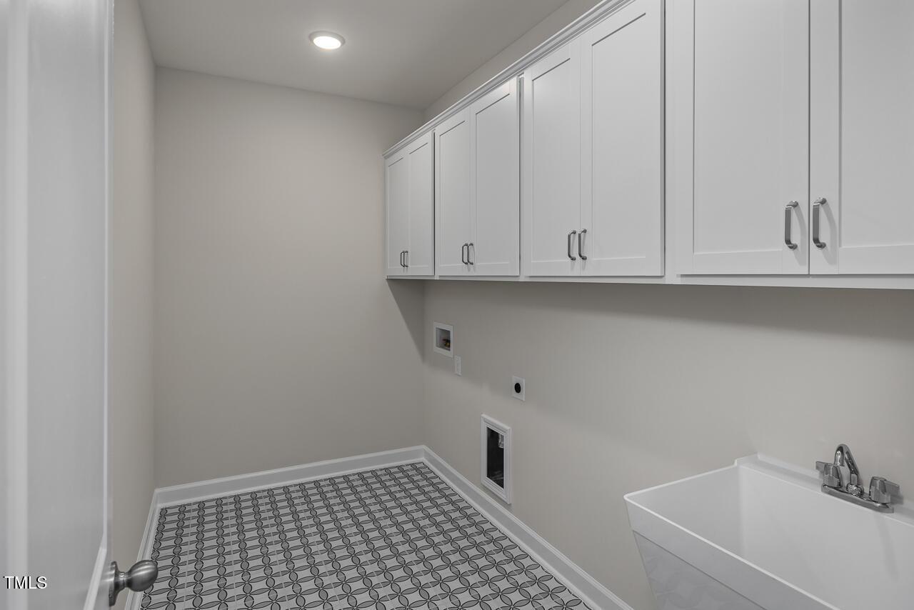 Functional laundry room with white upper cabinets, deep utility sink, washer-dryer hookups, and checkered tile floor in Davidson Homes The Aspen B, Wake Forest, NC