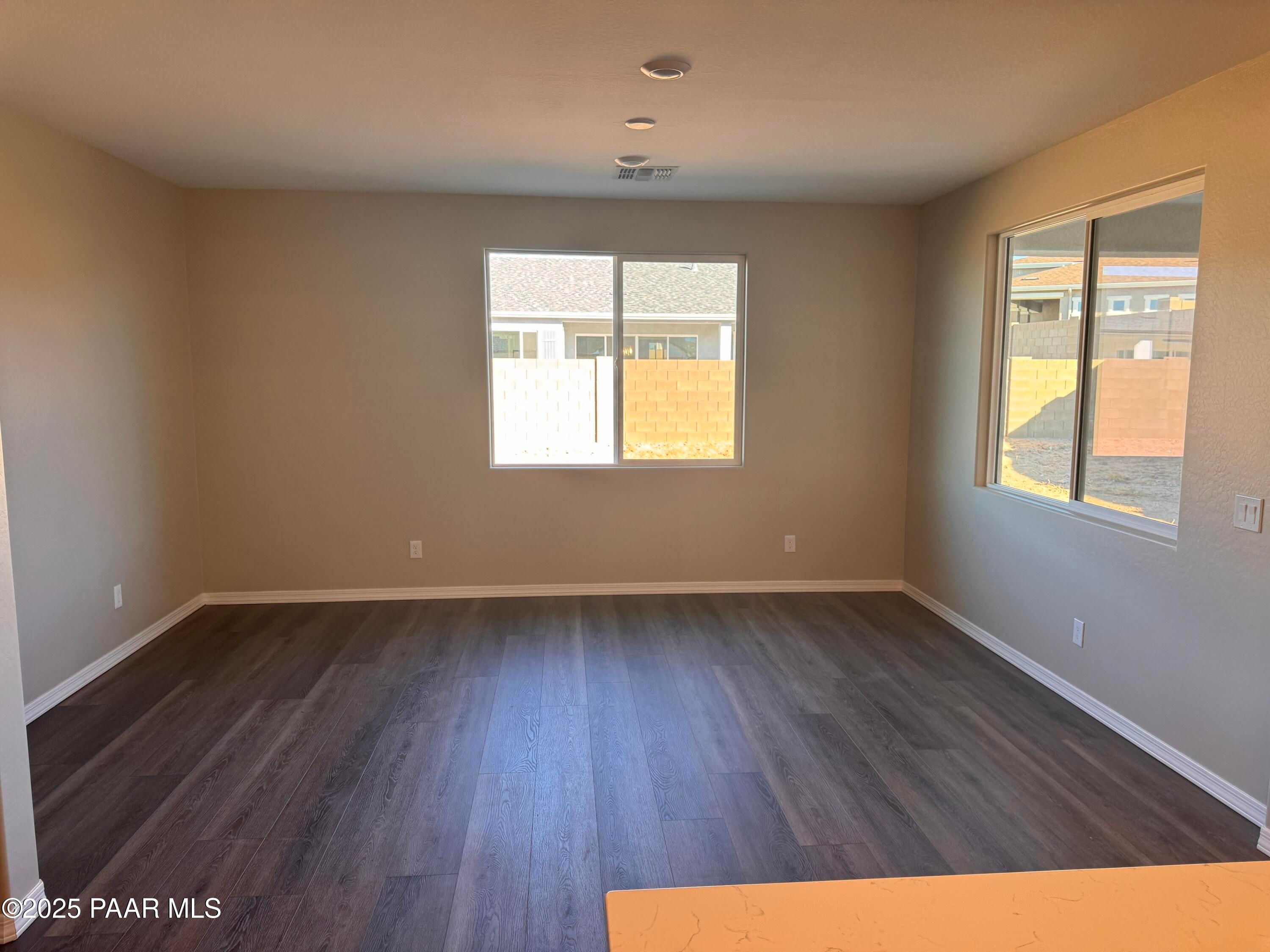 Spacious empty living room with beige walls, dark laminate flooring, large windows overlooking block wall and neighbor in Davidson Homes Sunrise II A, Prescott AZ