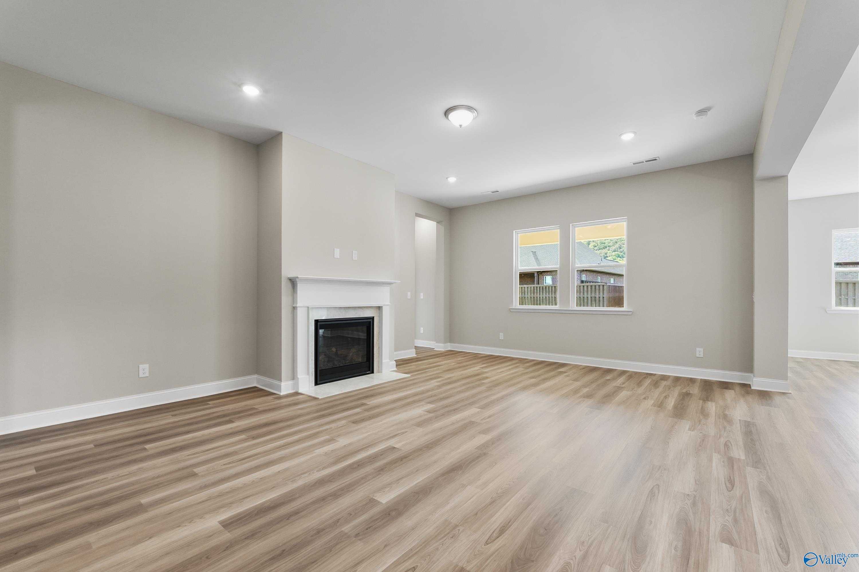Cozy family room featuring white gas fireplace, hardwood floors, and neutral walls in Evermore Homes The Haven, Owens Cross Roads, Alabama